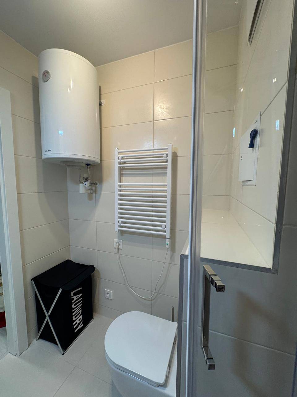 Kleines, gefliestes Badezimmer mit Toilette, Duschkabine und beheiztem Handtuchhalter.