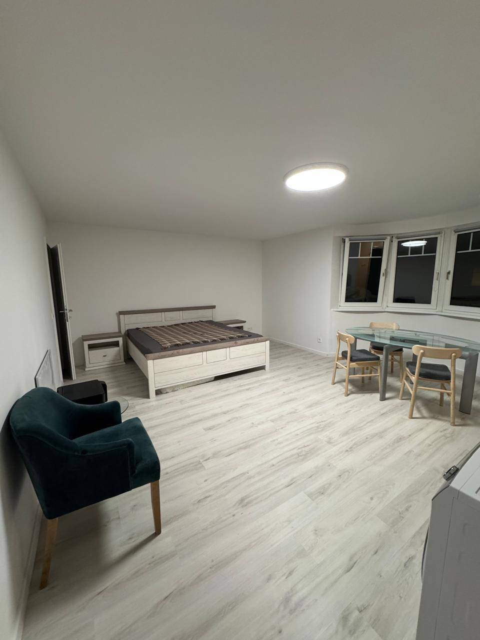 Geräumiger, heller Raum mit Bett, Esstisch und großen Fenstern, ausgestattet mit modernem Laminatboden.