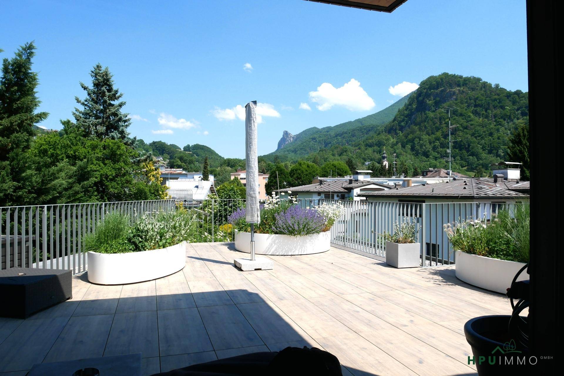 Sonniger Terrassenbereich mit Blumenkübeln und Panoramablick auf die Berge und Stadt.