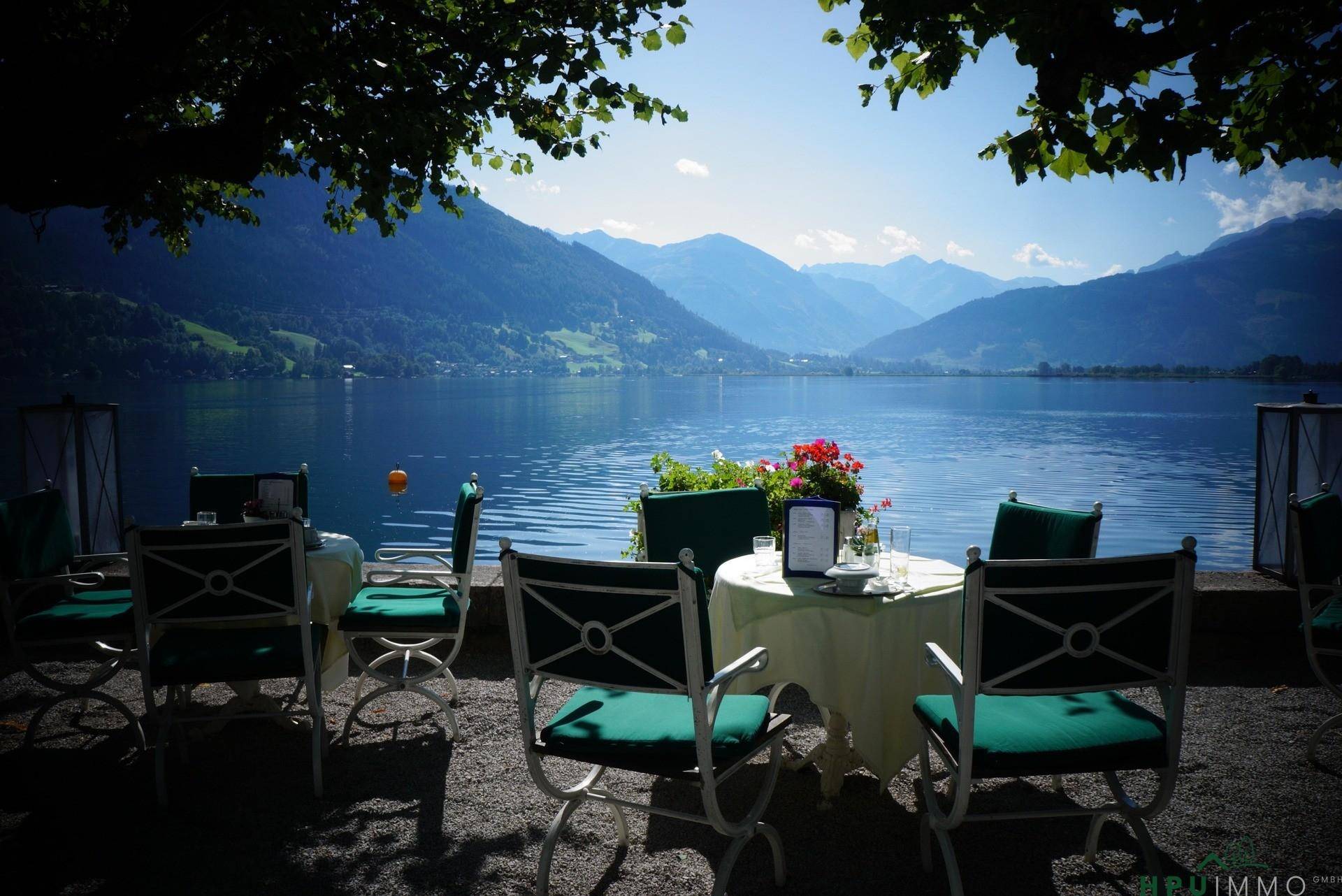 Idyllische Terrasse mit Seeblick und Bergpanorama, umgeben von Bäumen und eleganten Sitzgelegenheiten.