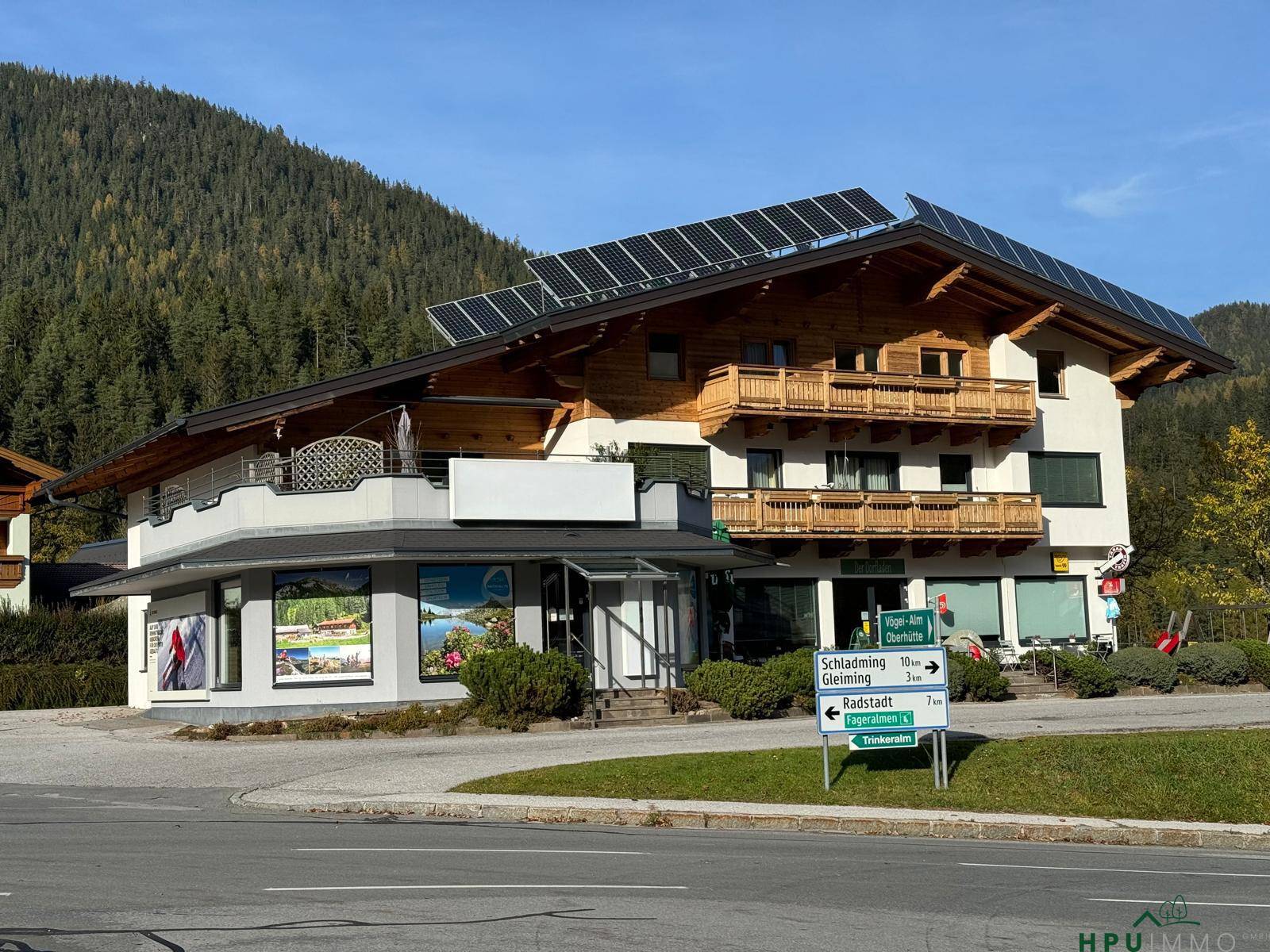 Gebäude mit Solaranlage auf dem Dach, umgeben von Bergen und grüner Landschaft im Herbst.