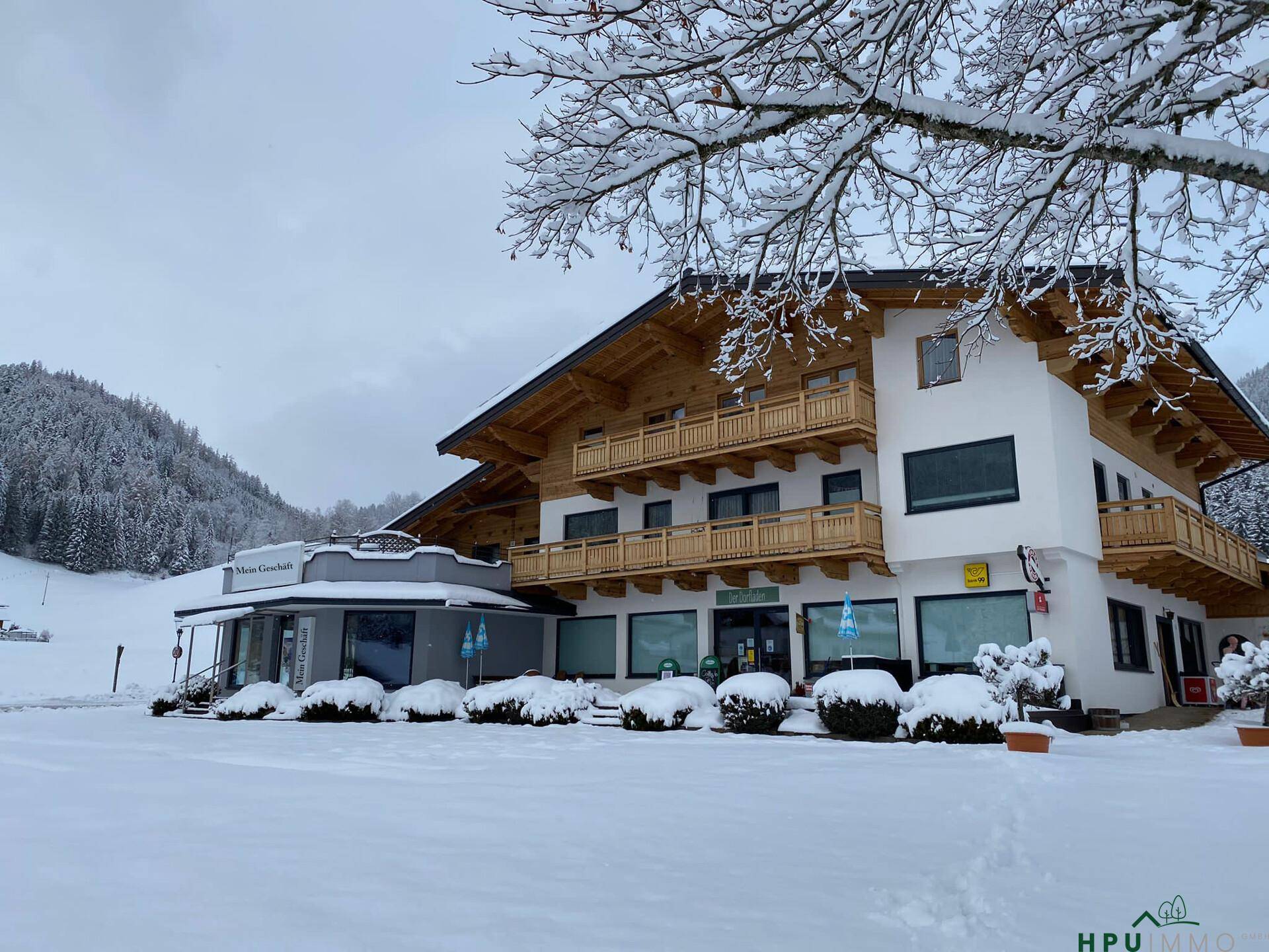 Winterliche Außenansicht des Gebäudes mit verschneiter Umgebung und Bergen im Hintergrund.