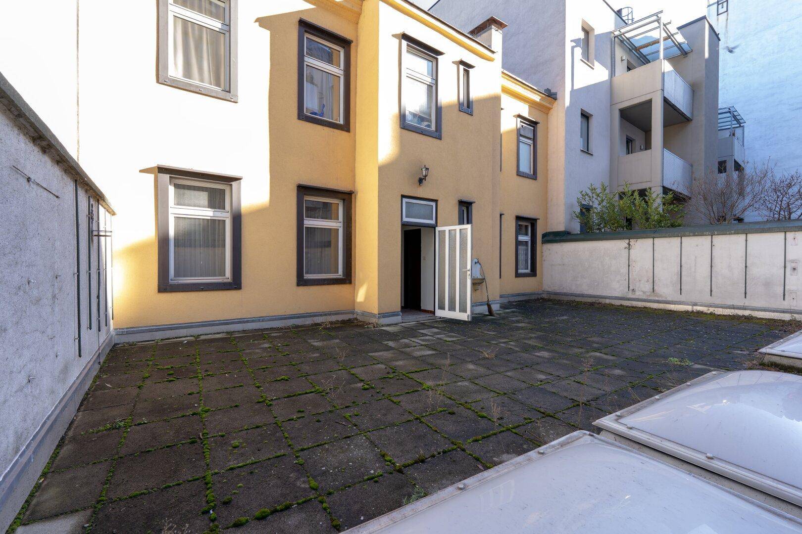 Gepflasterter Außenbereich hinter dem Gebäude mit Potenzial für eine Terrasse oder einen Garten.