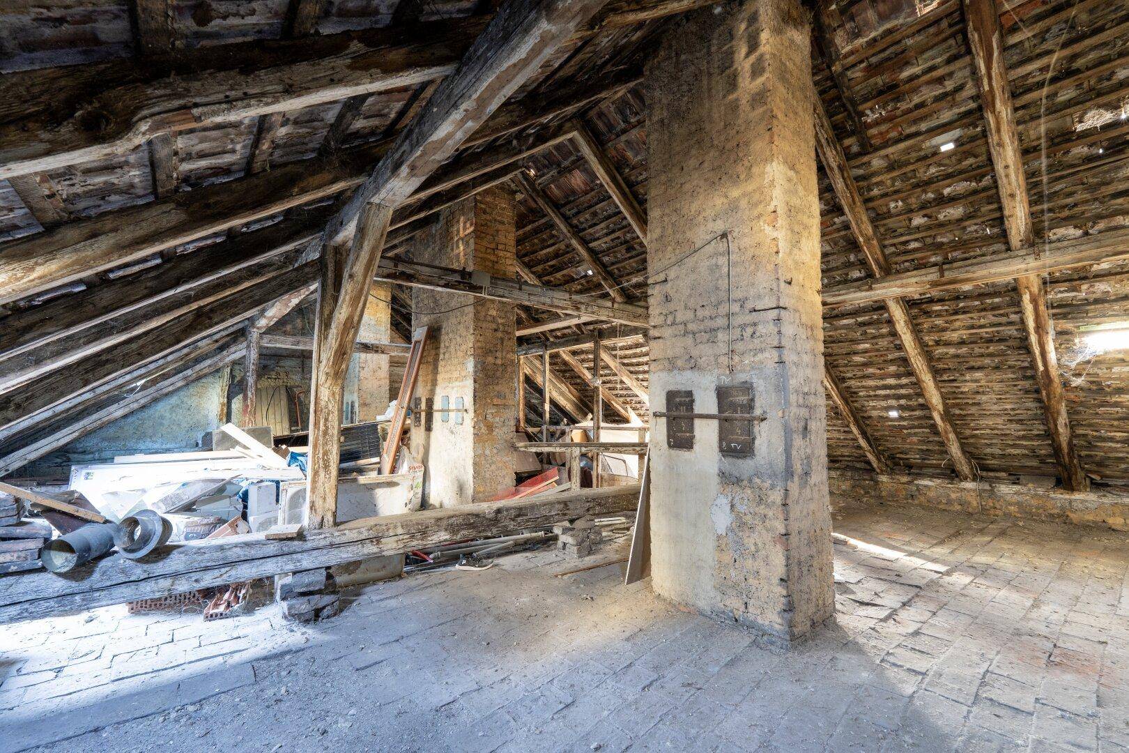 Geräumiger Dachboden mit freiliegenden Holzbalken und Ziegelpfeilern, bereit für den Ausbau.