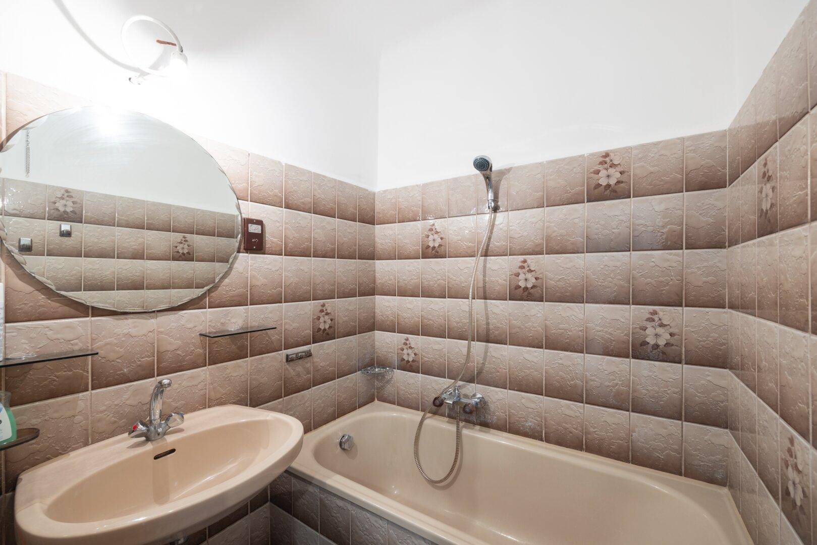 Badezimmer mit Badewanne, Waschbecken, rundem Spiegel und braunen Wandfliesen im Retro-Stil.