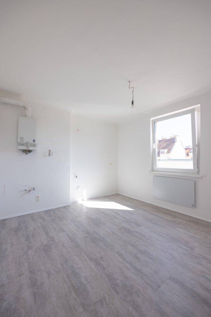 Leerer Raum mit Fenster, grauem Vinylboden und Anschlüssen für eine Küche oder Hauswirtschaftsraum.