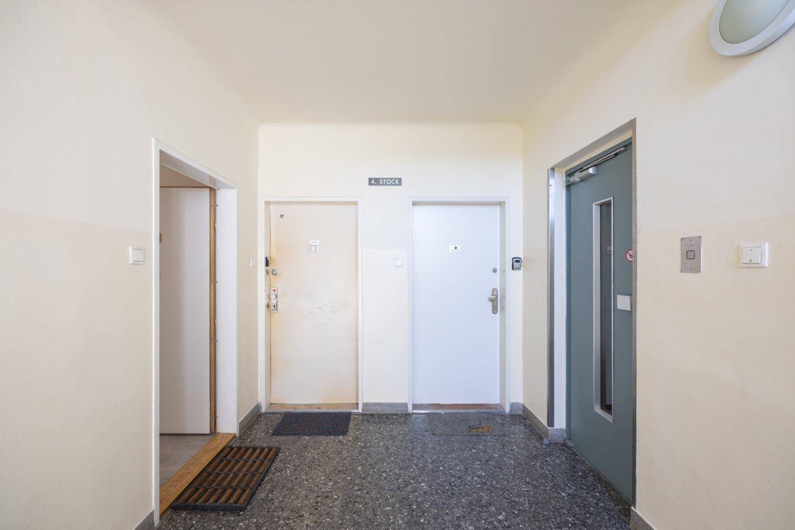 Gemeinschaftlicher Flur im Obergeschoss mit mehreren Wohnungstüren und einem Aufzug.