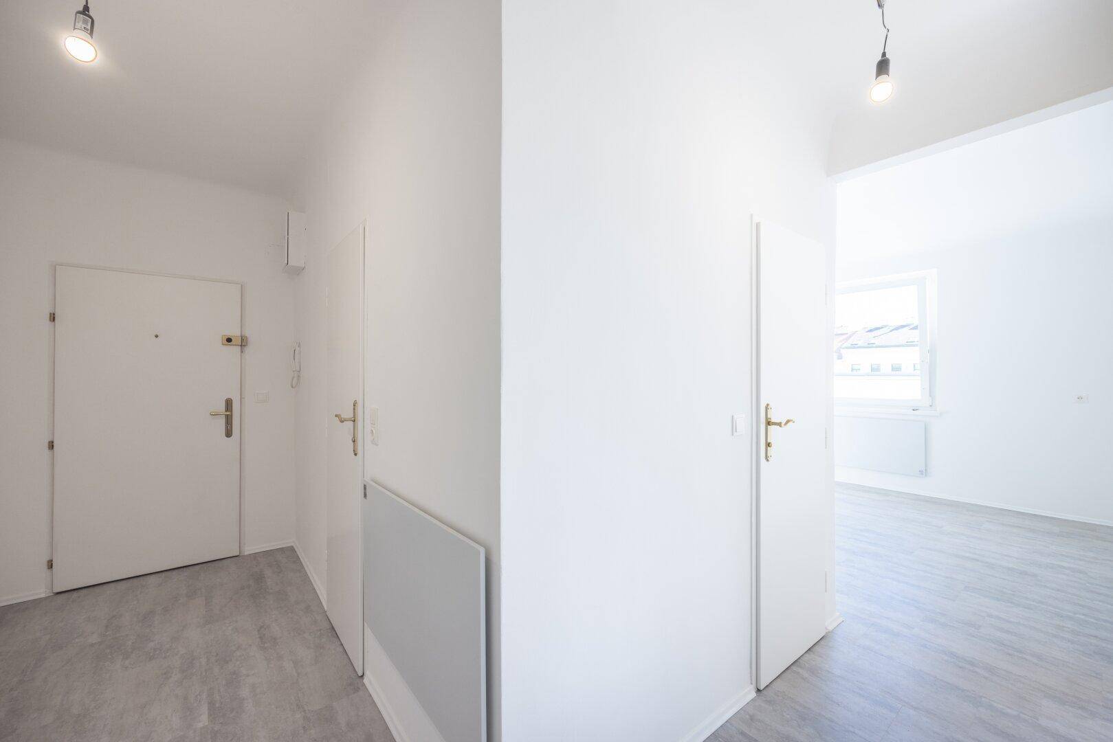 Heller Flur mit weißen Türen und einem Durchgang zu einem weiteren Raum mit Fenster.