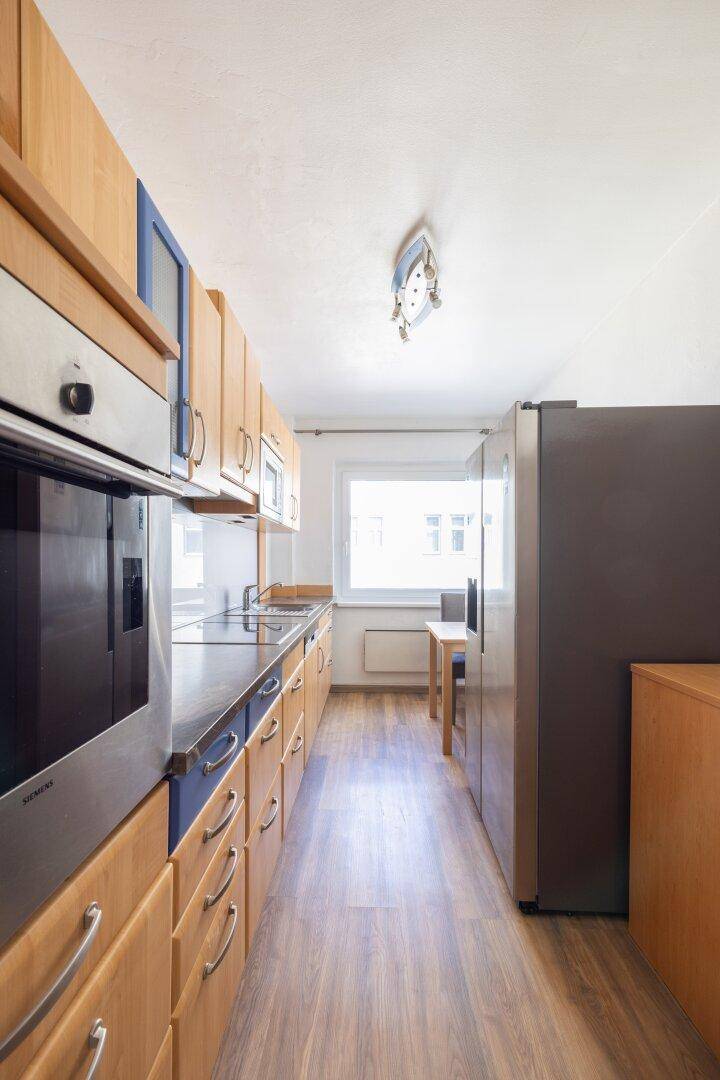 Funktionale Küche mit Holzschränken, dunklen Arbeitsplatten und modernen Edelstahlgeräten.