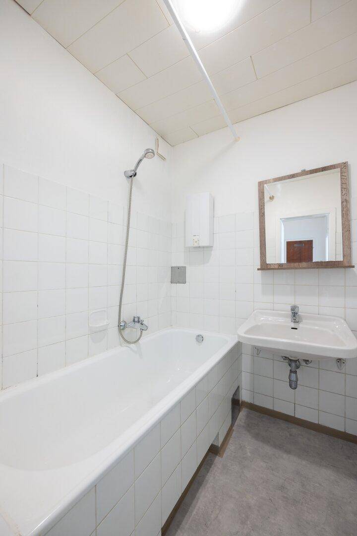 Helles Badezimmer mit weißen Fliesen, Badewanne mit Duschfunktion und Waschbecken.