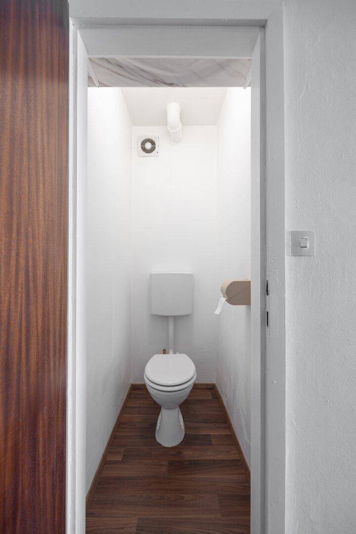 Kleines, separates WC mit Toilette und Holzboden, einfach und funktional.