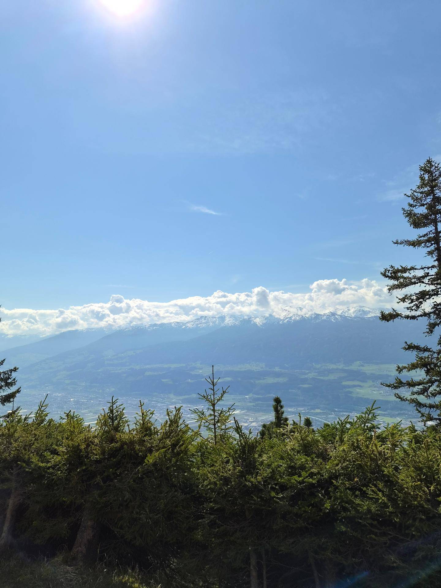 Panoramablick auf schneebedeckte Berge und ein weites Tal unter blauem Himmel.