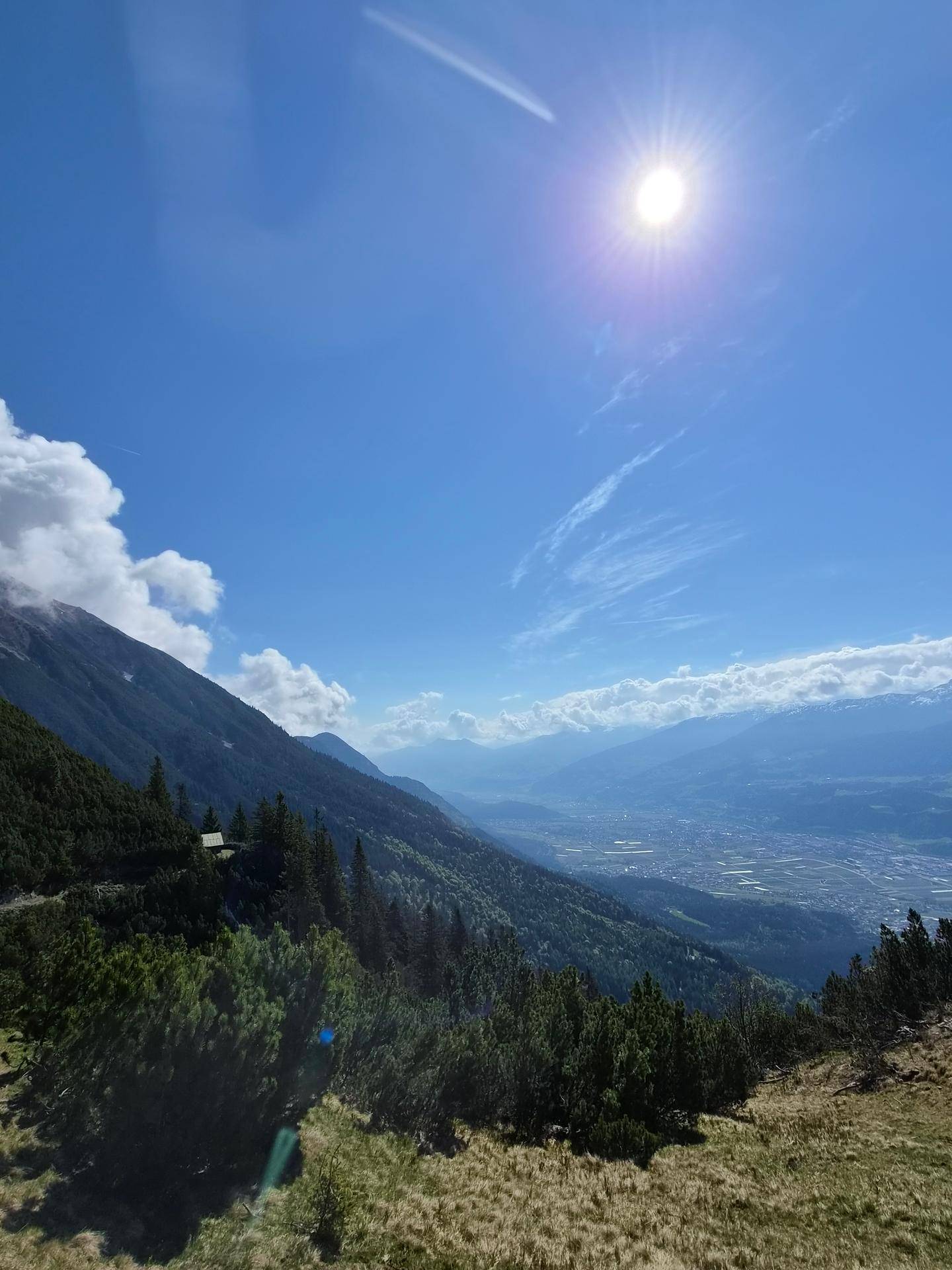 Ein weitreichender Panoramablick über ein sonniges Bergtal mit einer Stadt in der Ferne.