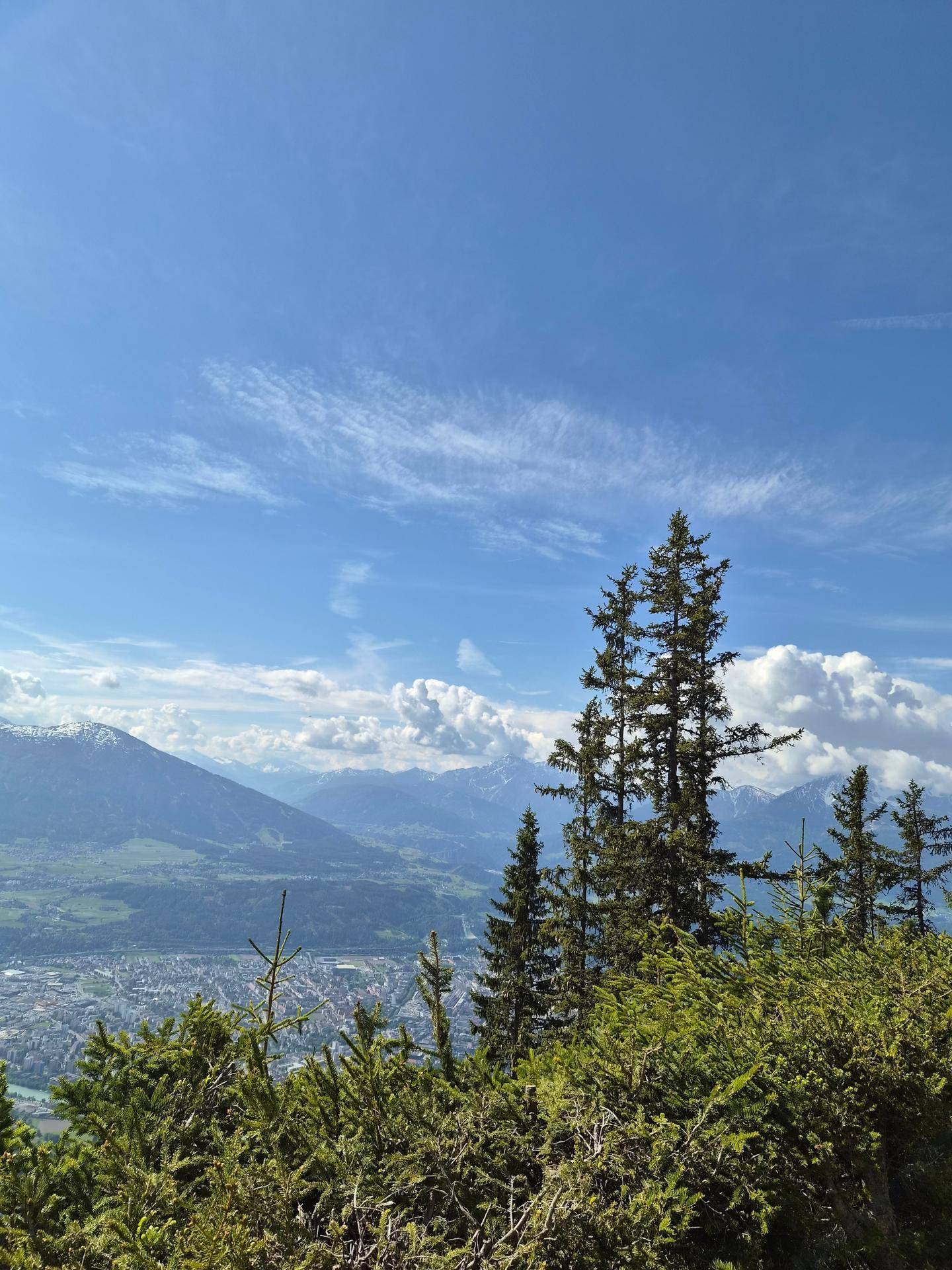 Weitblick über ein Tal mit einer Stadt und schneebedeckten Bergen im Hintergrund.