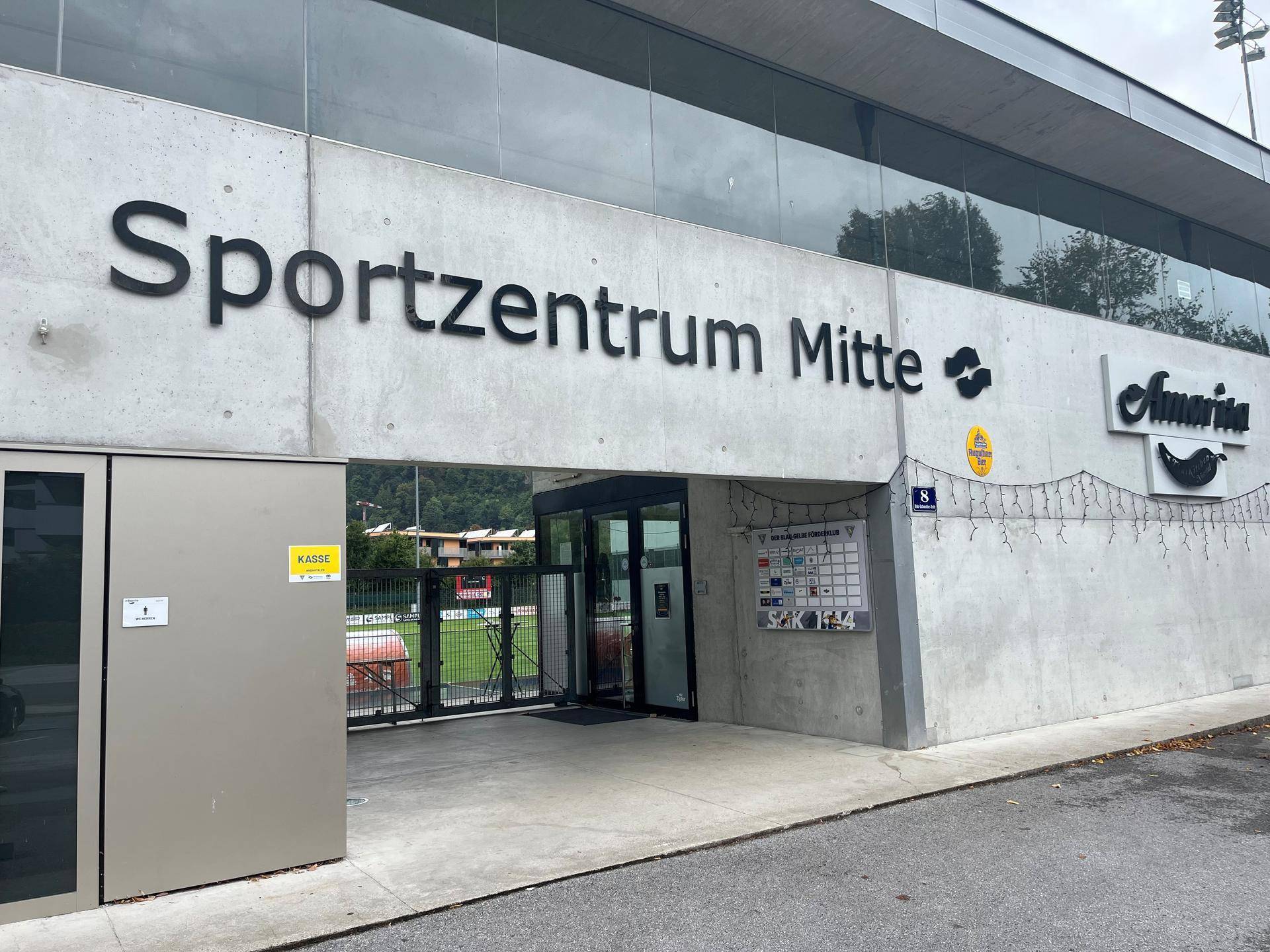 Eingangsbereich des Sportzentrums Mitte mit Betonfassade, großen Glasflächen und Beschilderung.