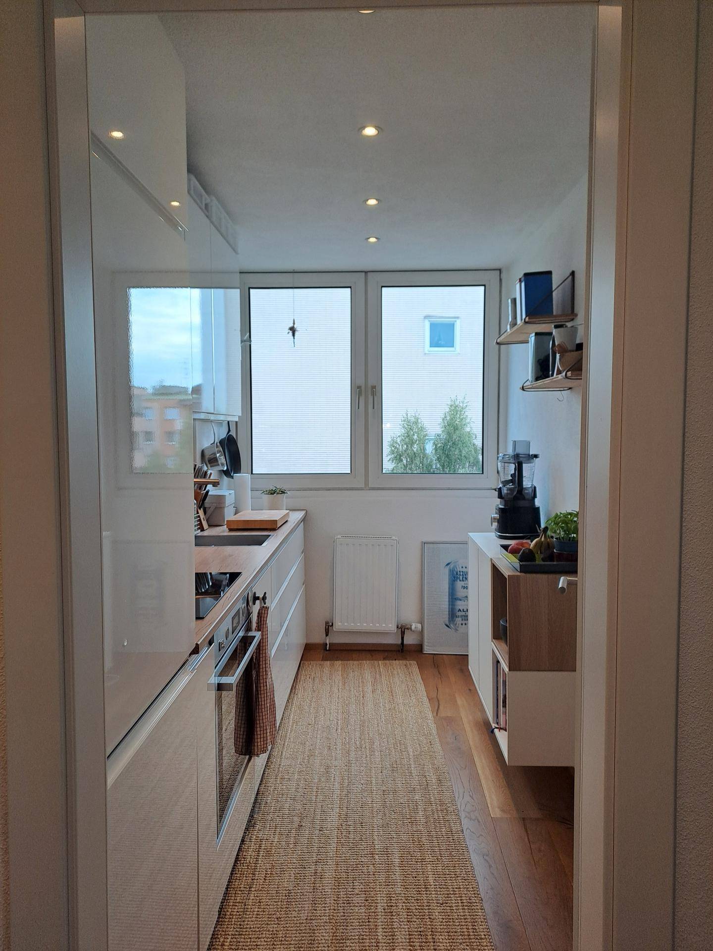 Schmale, moderne Küche mit Holzboden, Einbaugeräten und Fenster.