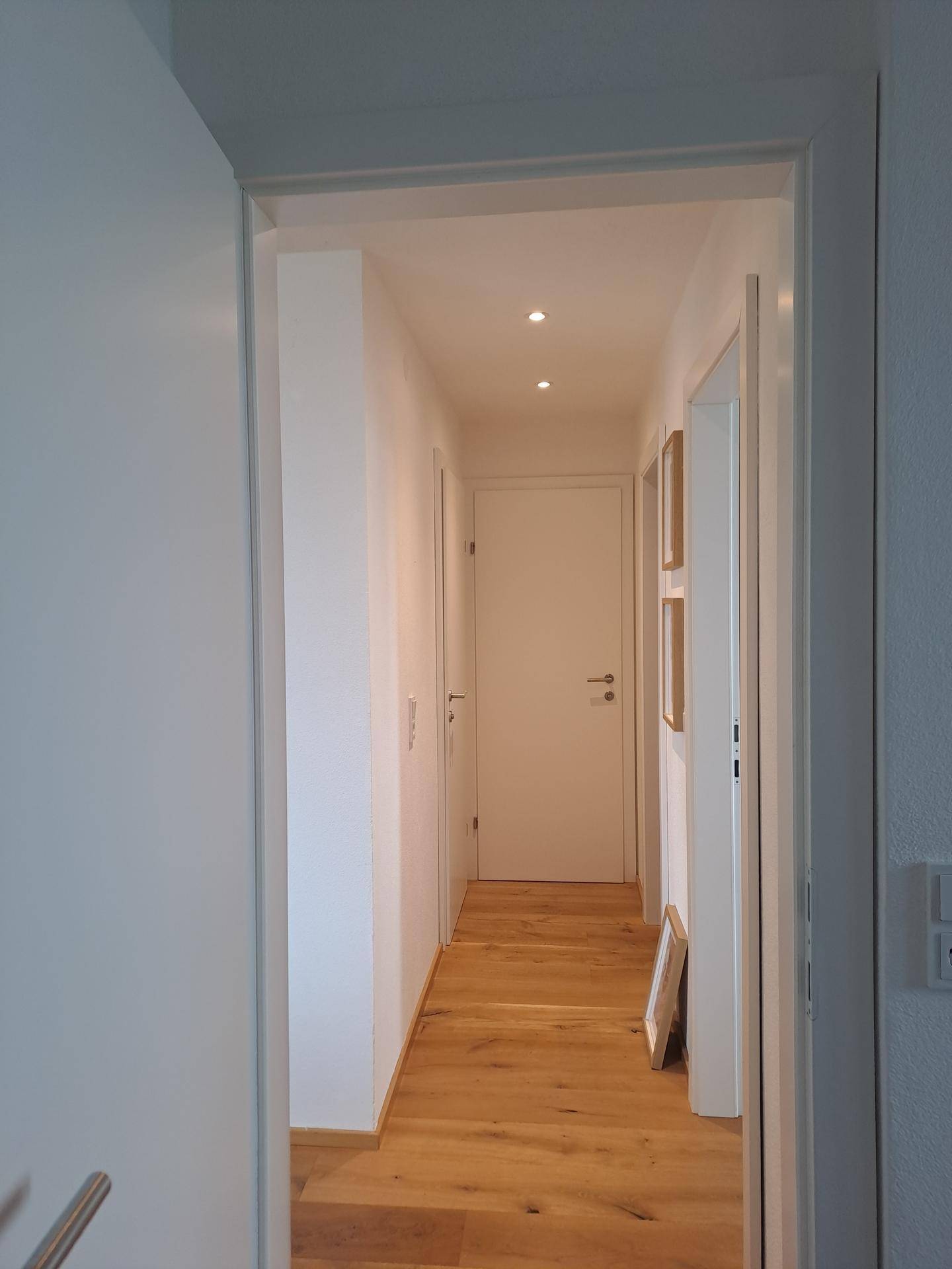 Heller Flur mit Holzboden und mehreren Türen, beleuchtet durch Deckenspots.
