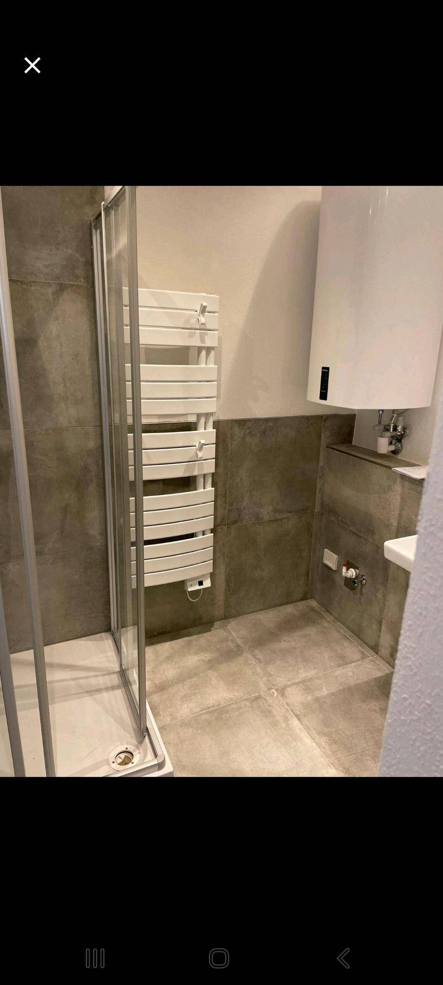 Badezimmer mit Duschkabine, beheiztem Handtuchhalter und grauen Fliesen.