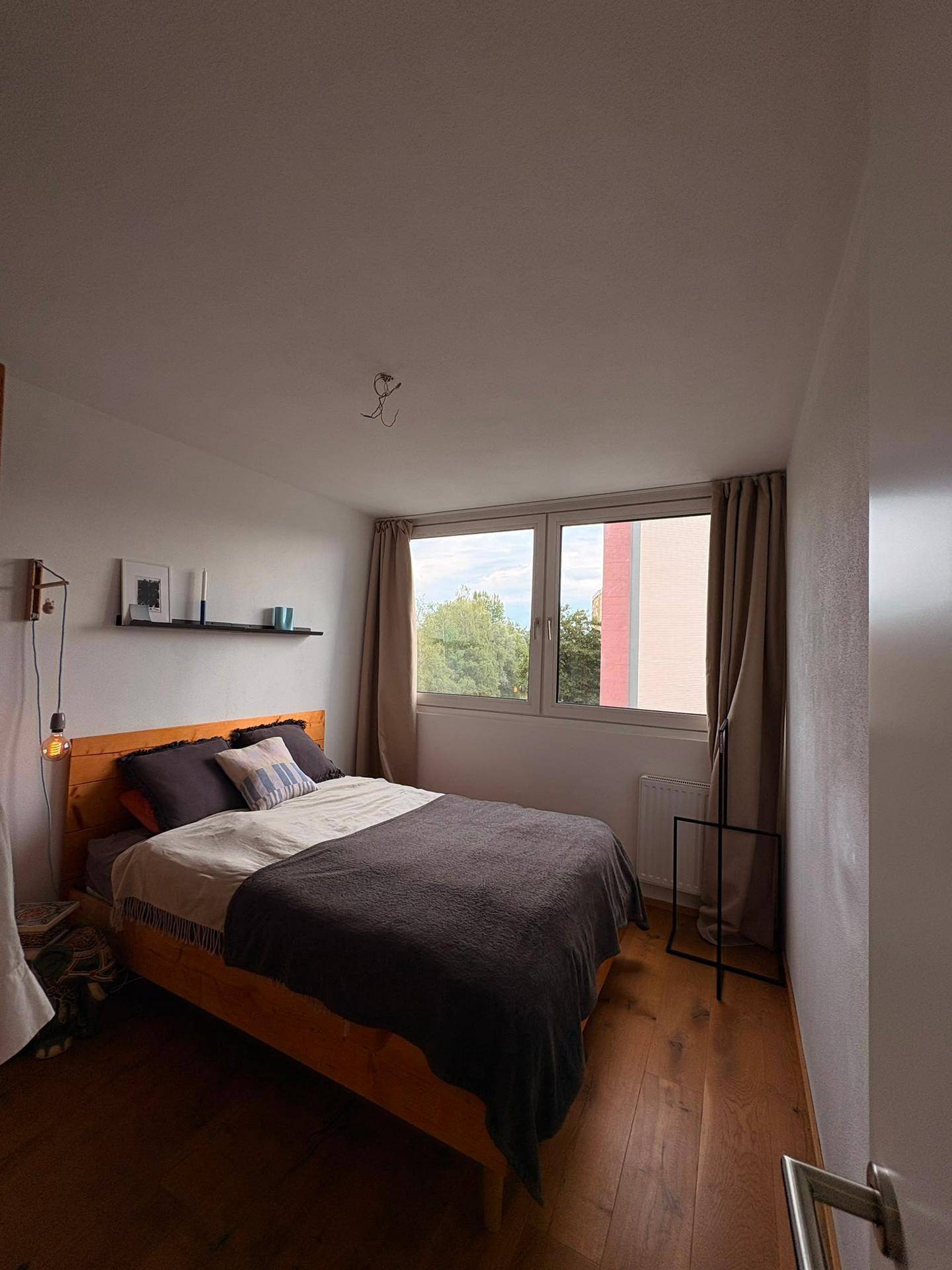 Gemütliches Schlafzimmer mit Holzbett, Holzboden und Fenster mit Blick ins Grüne.