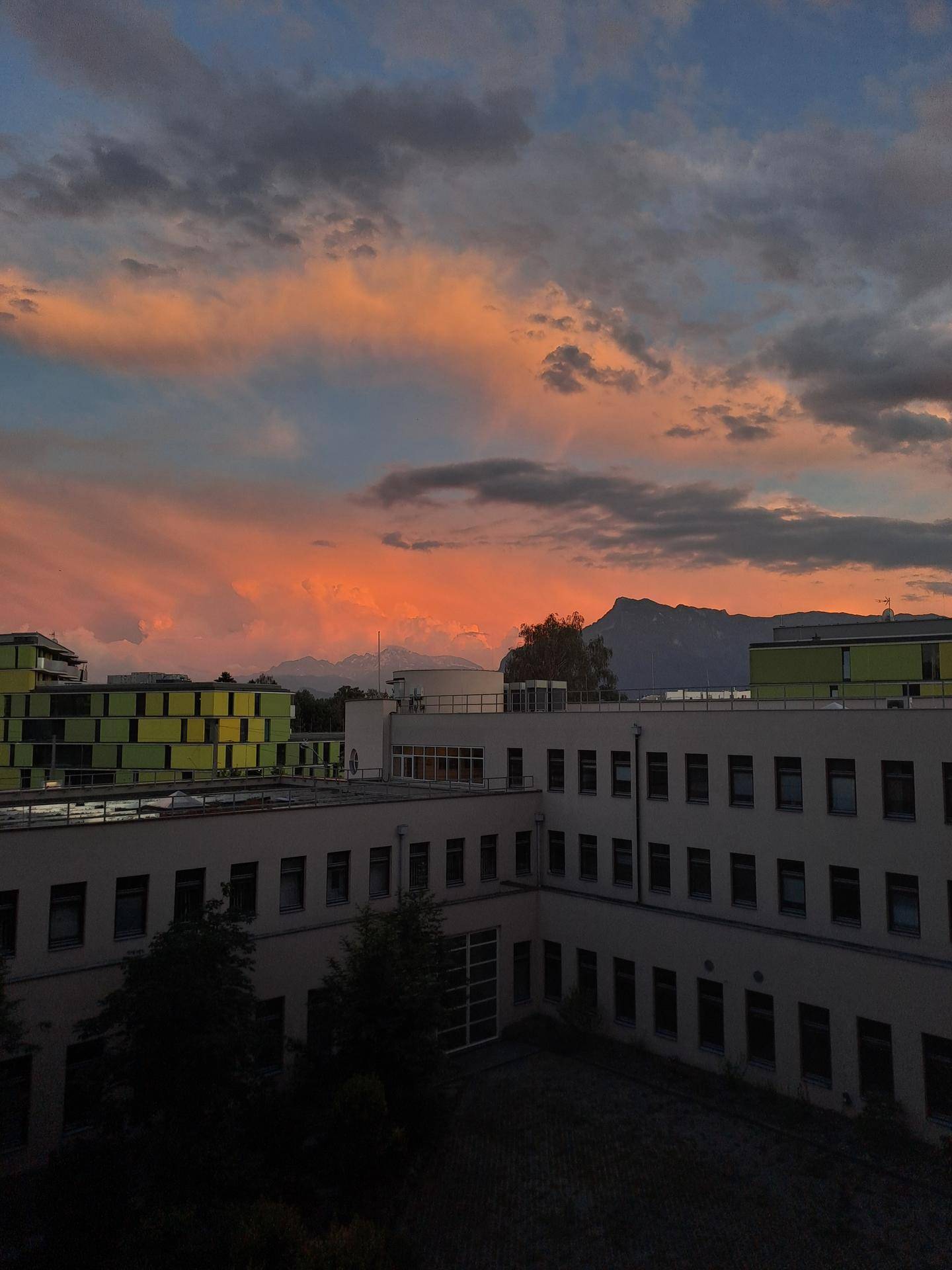 Abendlicher Blick über die Dächer der Stadt mit Bergen im Hintergrund und farbigem Himmel.