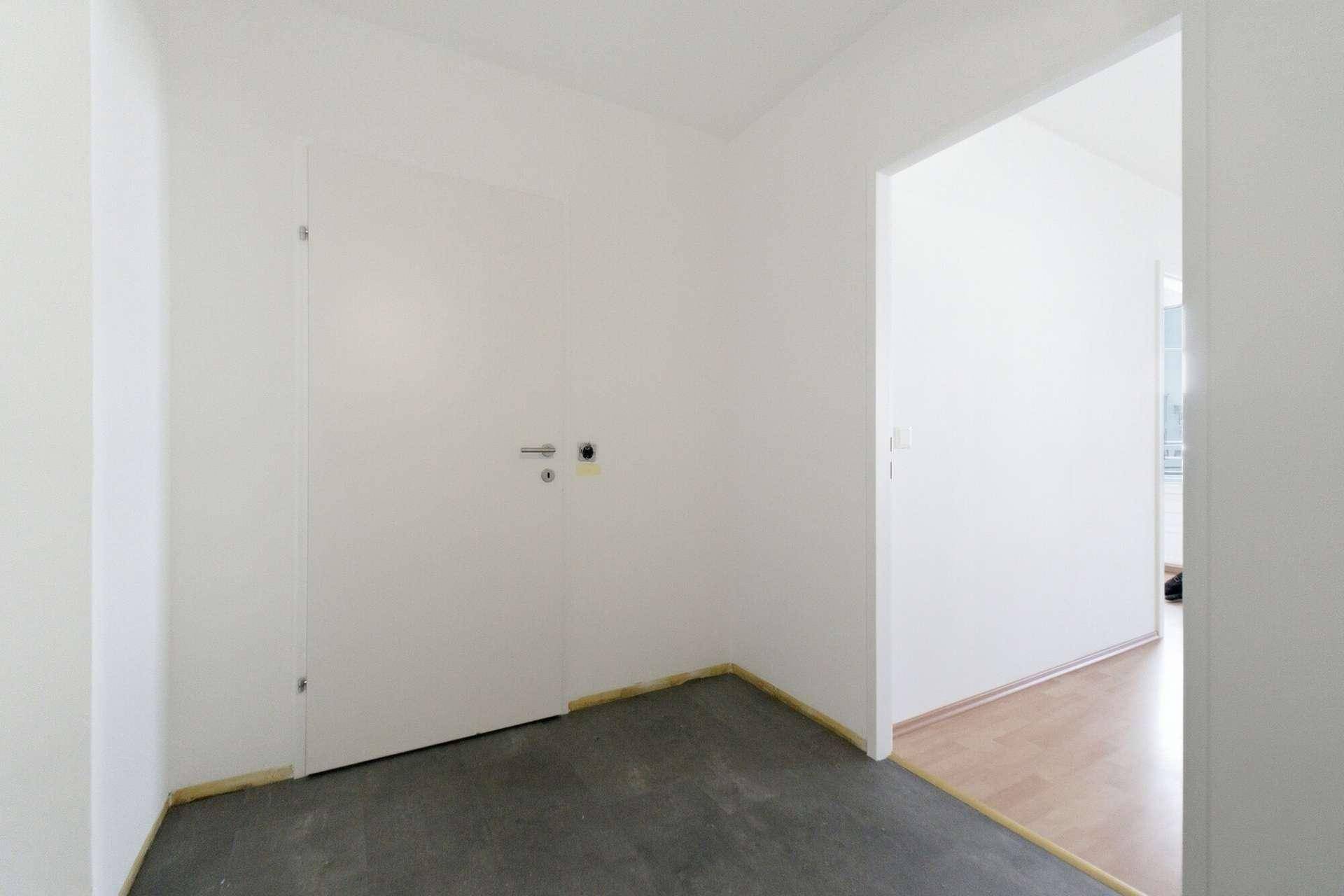 Heller Flur mit dunklem Boden und einer weißen Tür, die zu den Wohnräumen führt.
