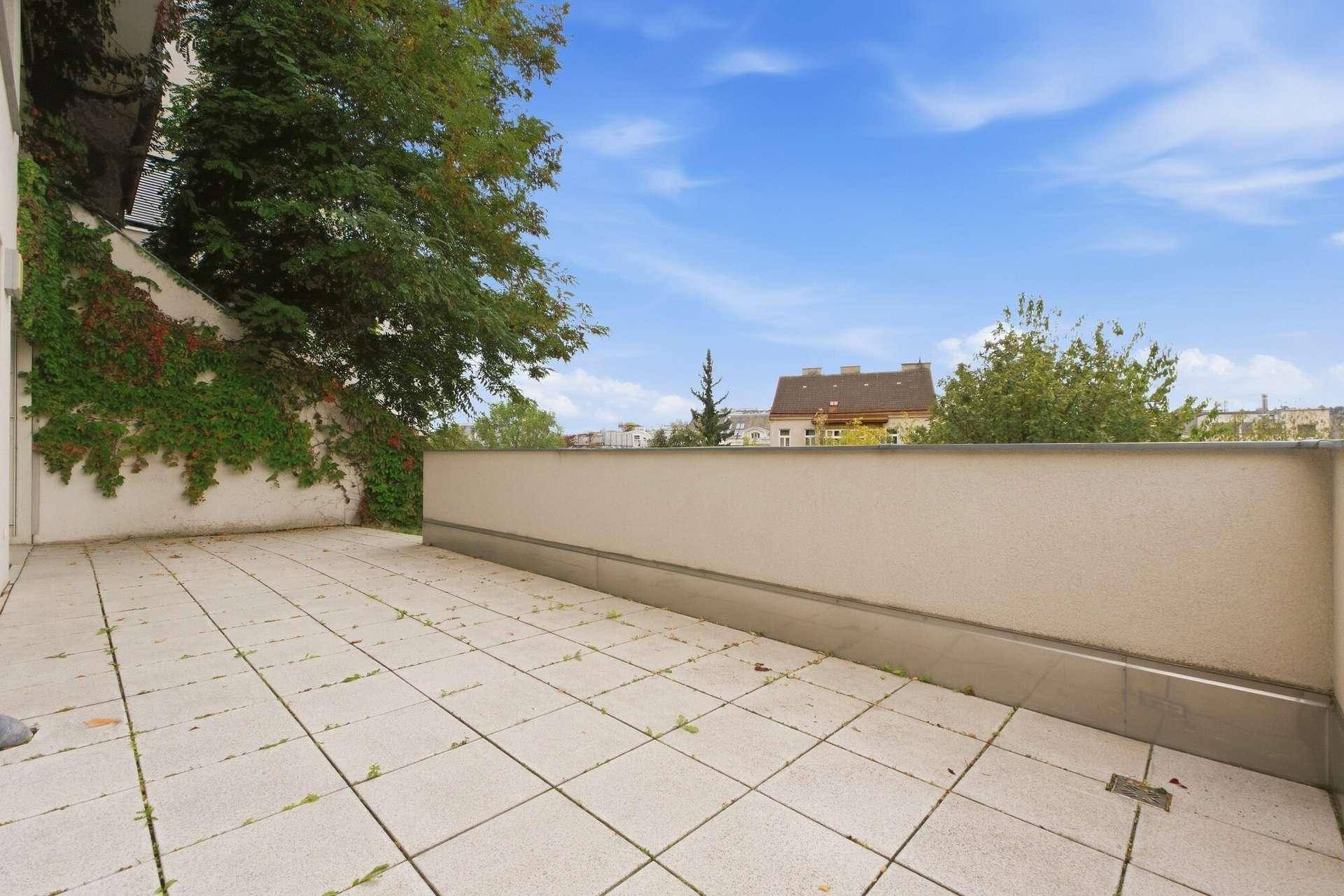 Geräumige Terrasse mit Fliesenboden, umgeben von Begrünung und mit Blick auf die Stadt.