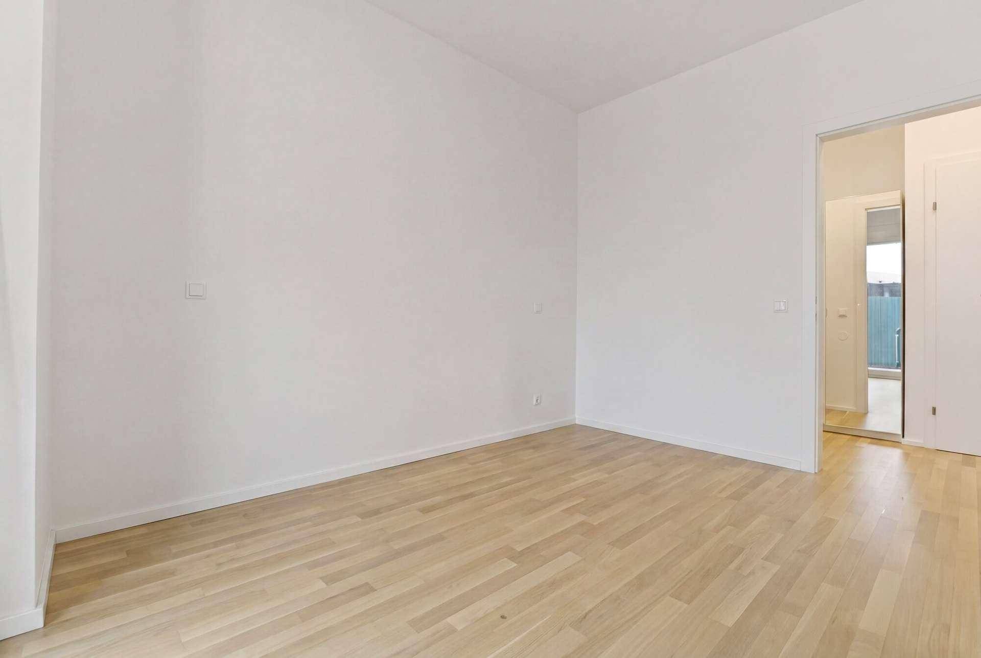Heller, leerer Raum mit Parkettboden und Zugang zu einem weiteren Zimmer.