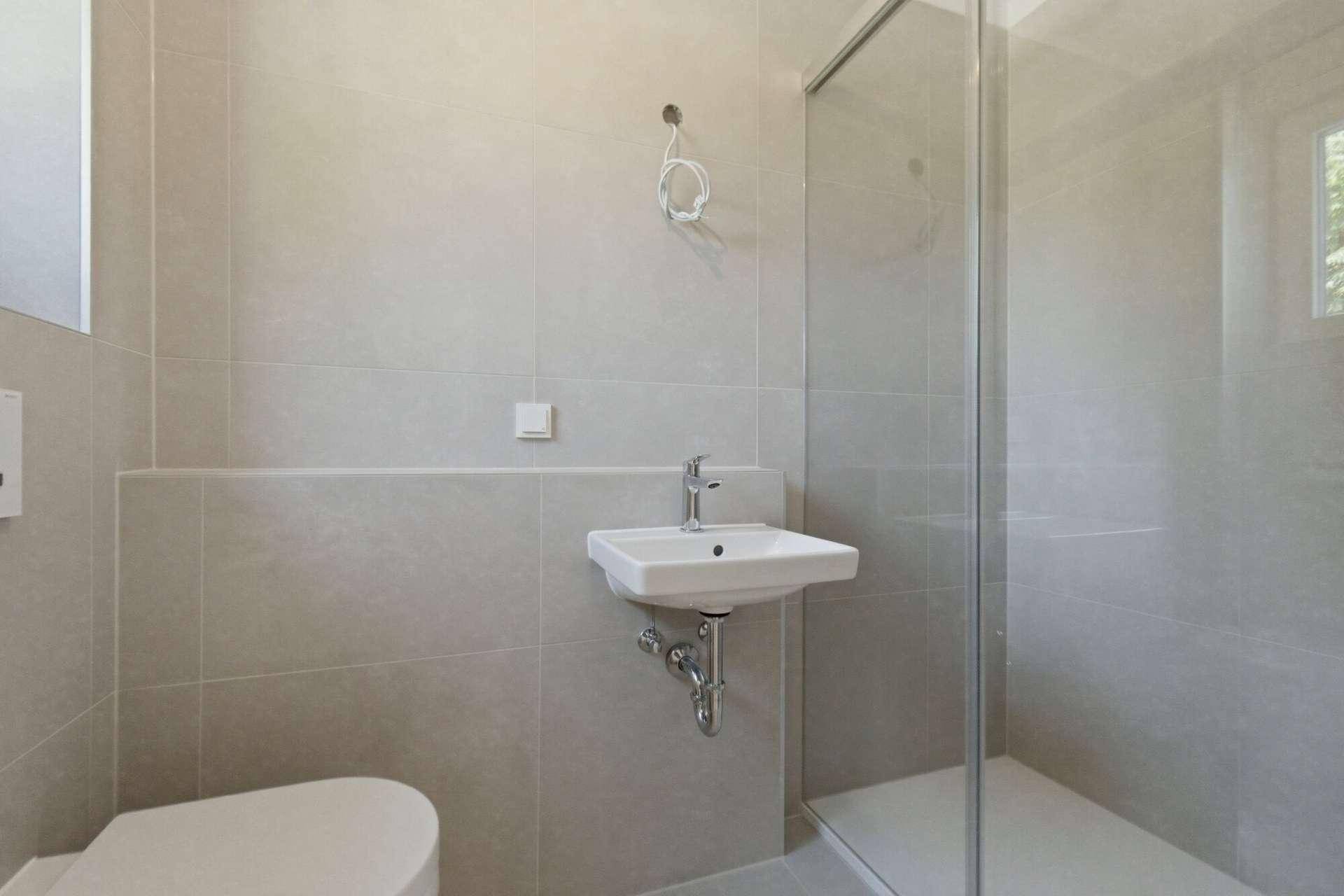 Kleines Gäste-WC mit Hänge-WC, Waschbecken und begehbarer Dusche, modern gefliest.