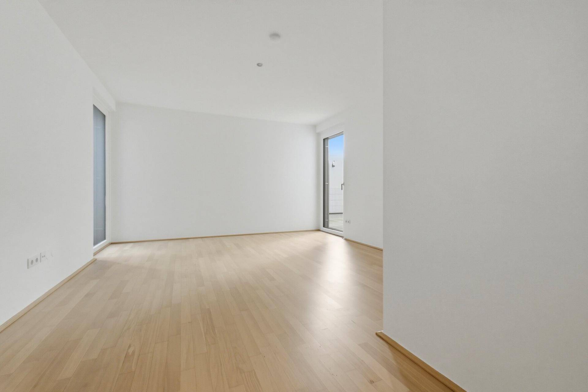 Leeres Zimmer mit hellem Holzboden und Zugang zu einem Außenbereich.