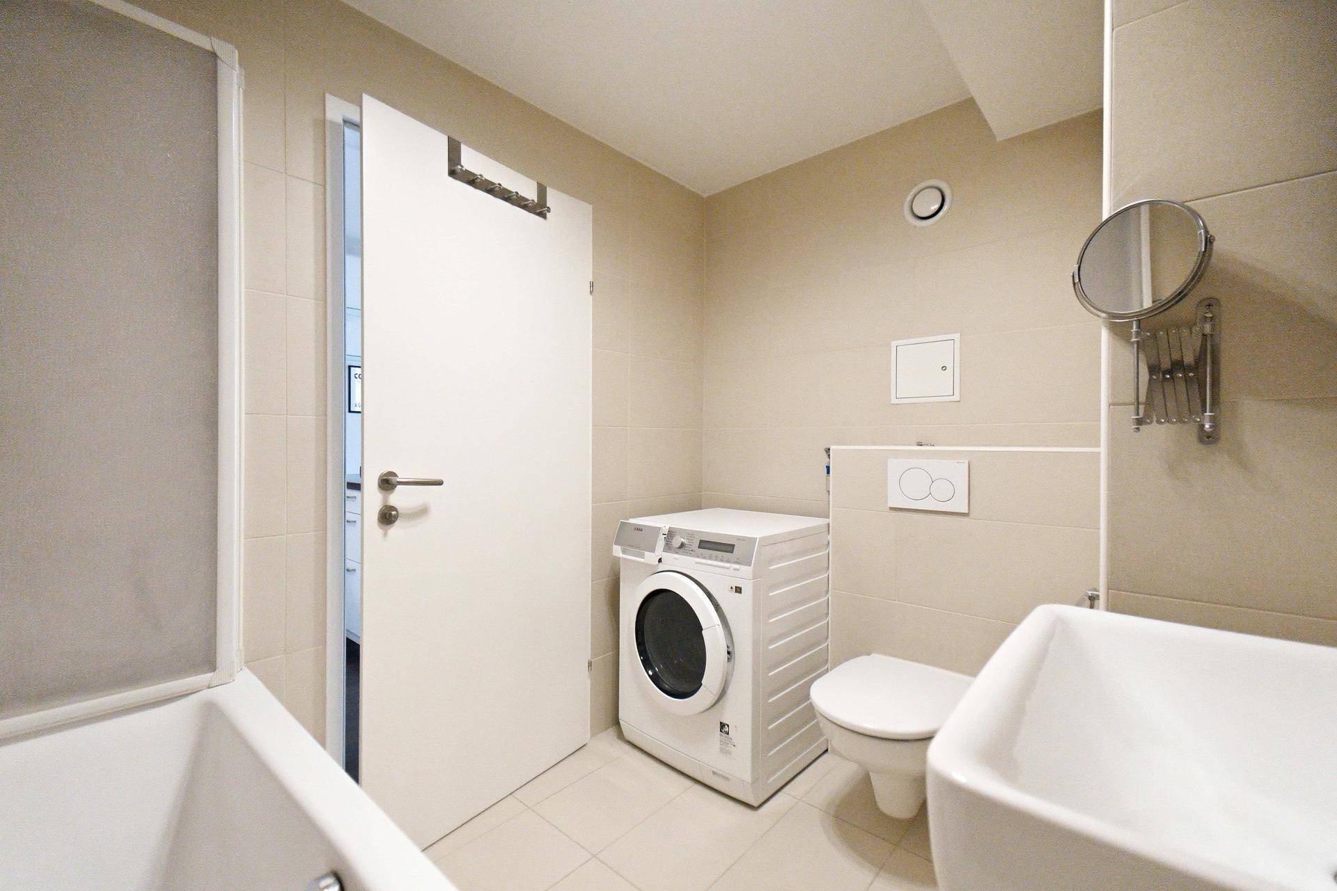 Modernes Badezimmer mit beigen Fliesen, Waschmaschine und Toilette, bietet praktische Ausstattung.