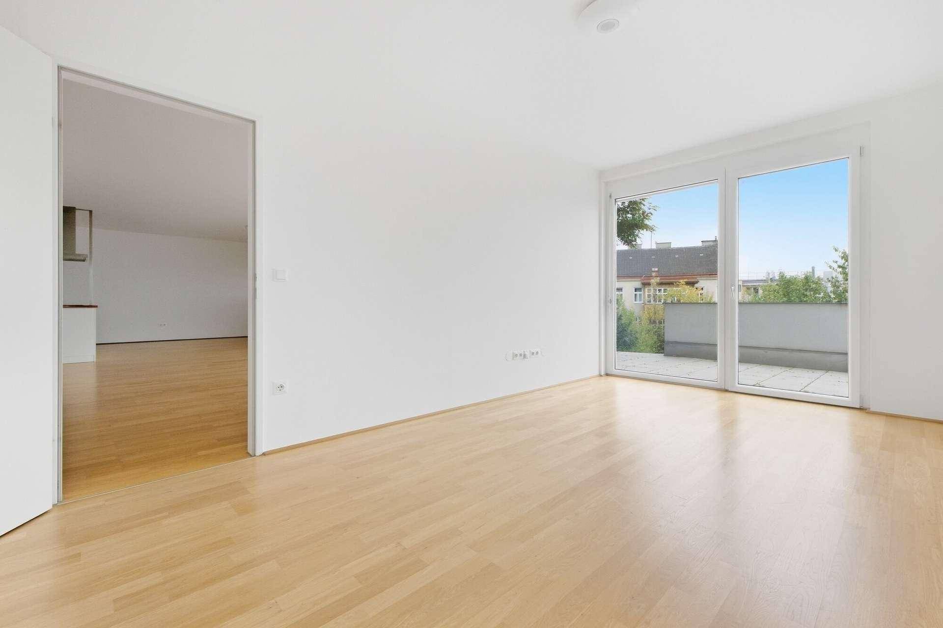 Helles Wohnzimmer mit Parkettboden, Blick in die Küche und Zugang zu einem Außenbereich.