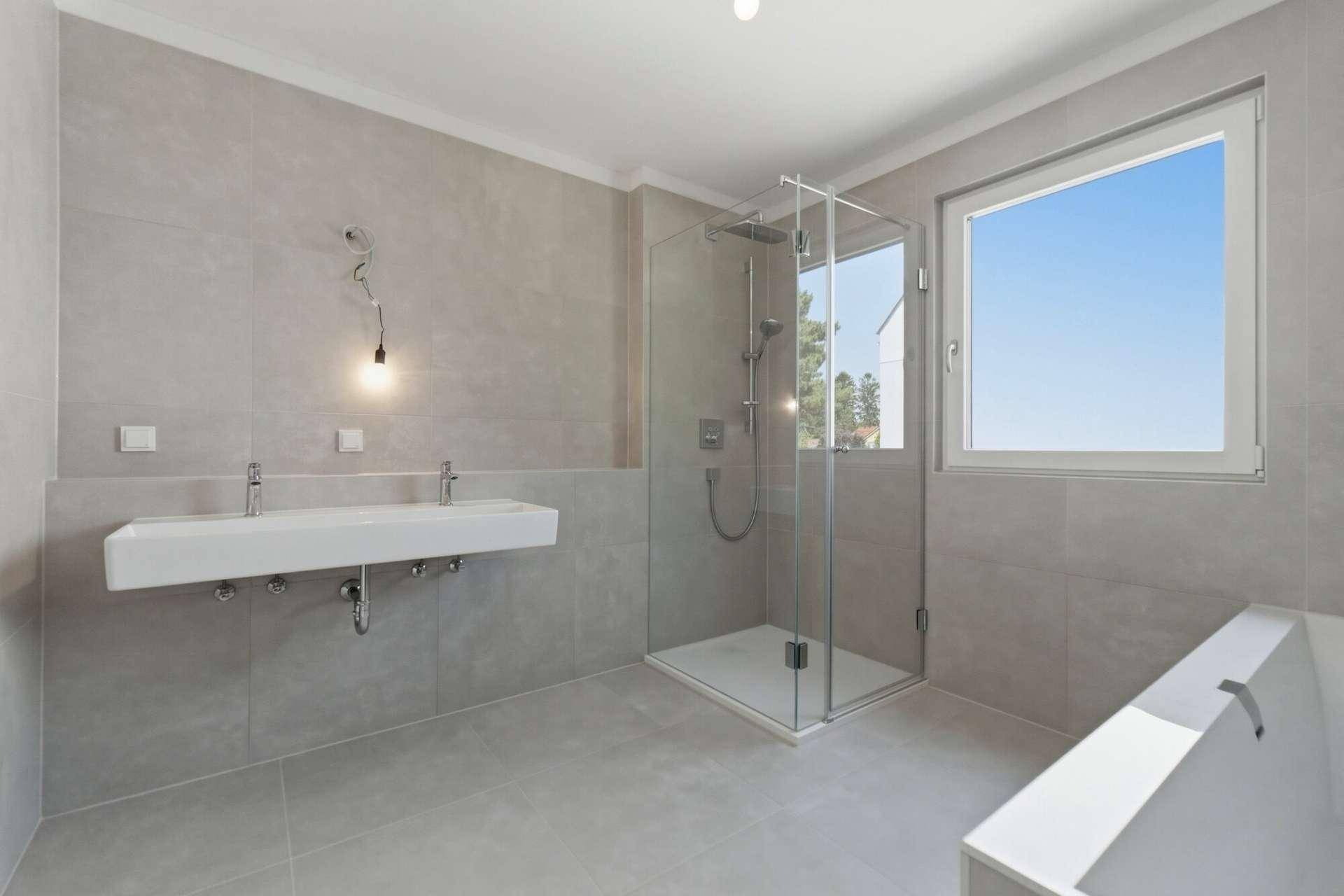 Helles Badezimmer mit Doppelwaschbecken, Badewanne, begehbarer Dusche und großem Fenster.