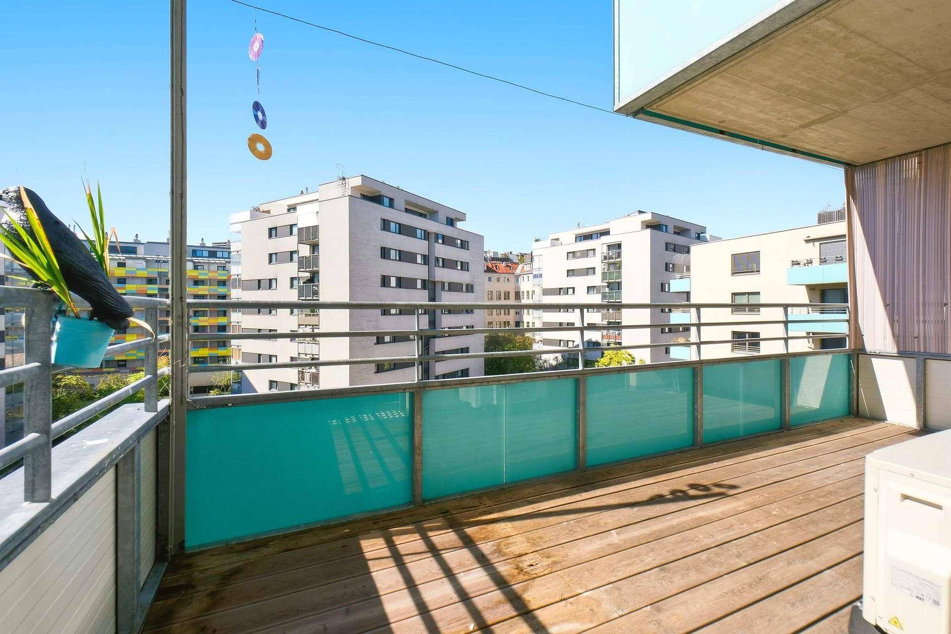 Geräumiger Balkon mit Holzdielen und Blick auf die moderne Stadtarchitektur.