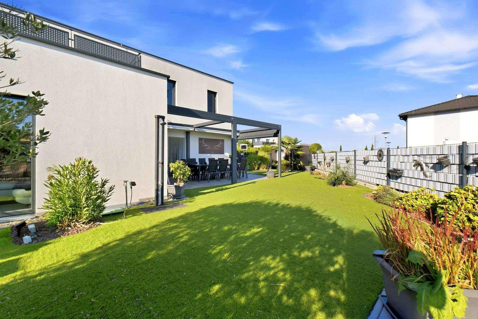 Rückansicht des modernen Hauses mit großem Garten und überdachter Terrasse.