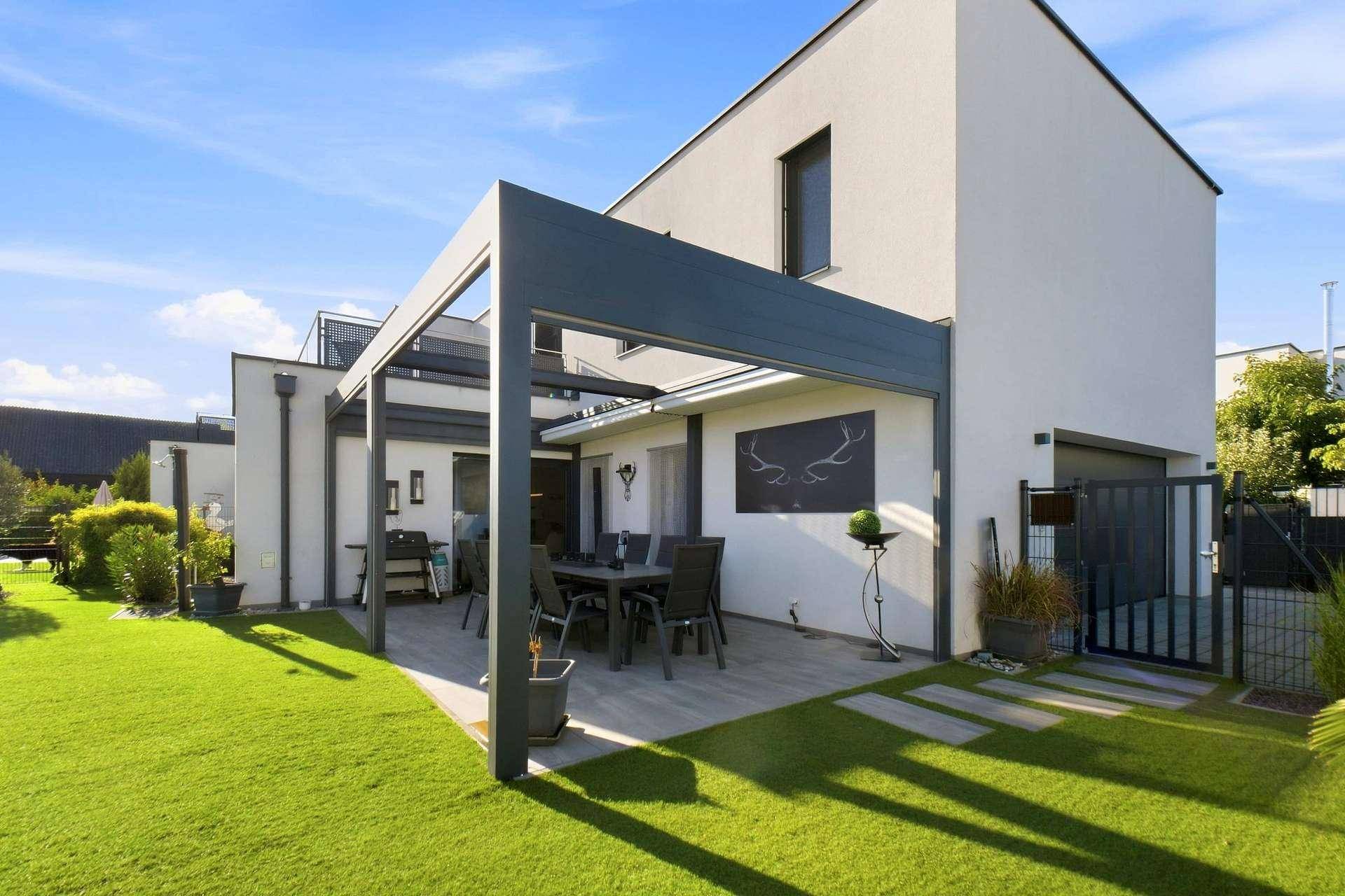 Überdachte Terrasse mit Essbereich und Zugang zum gepflegten Garten neben dem modernen Haus.