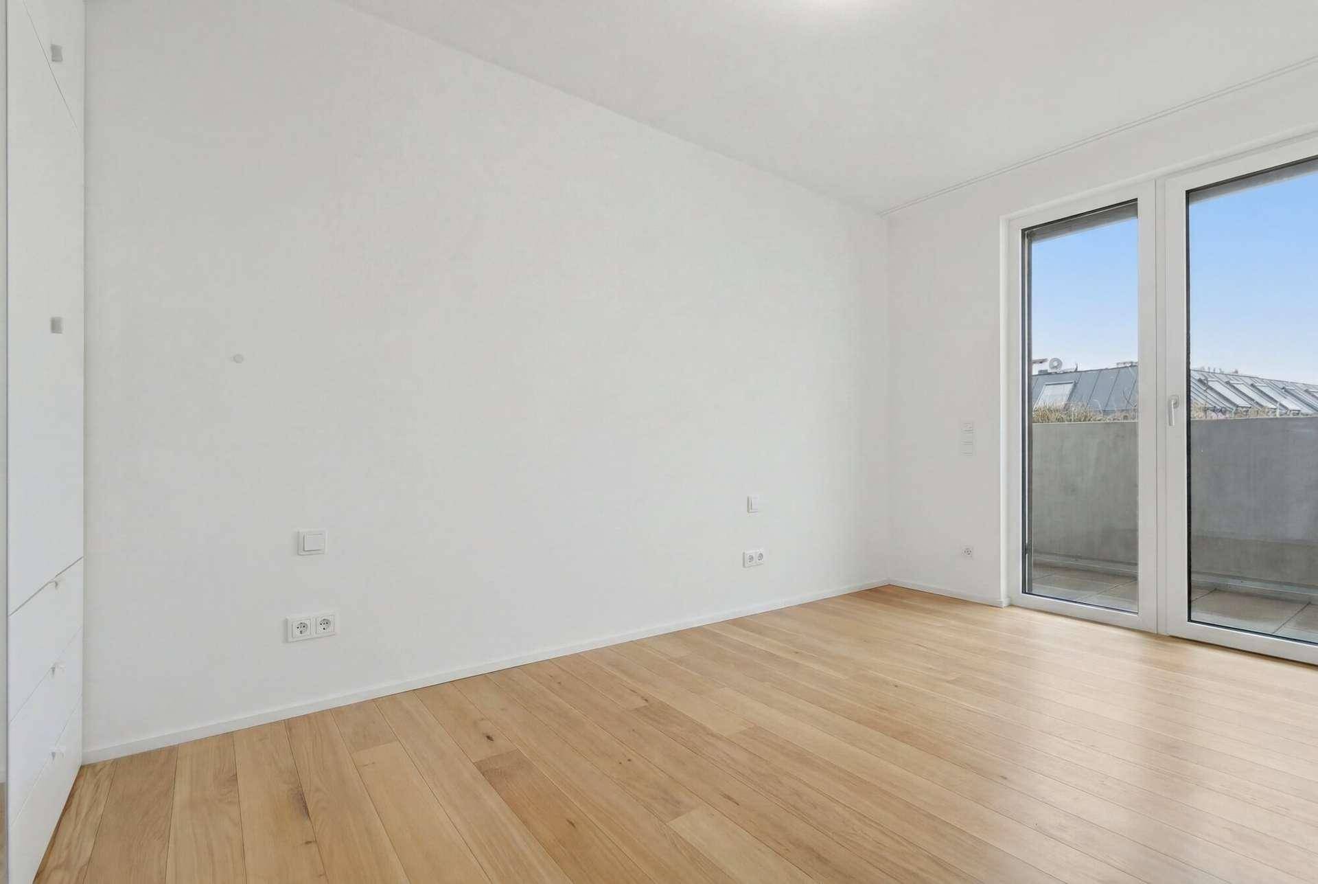 Helles Schlafzimmer mit Parkettboden und Zugang zu einem Außenbereich.