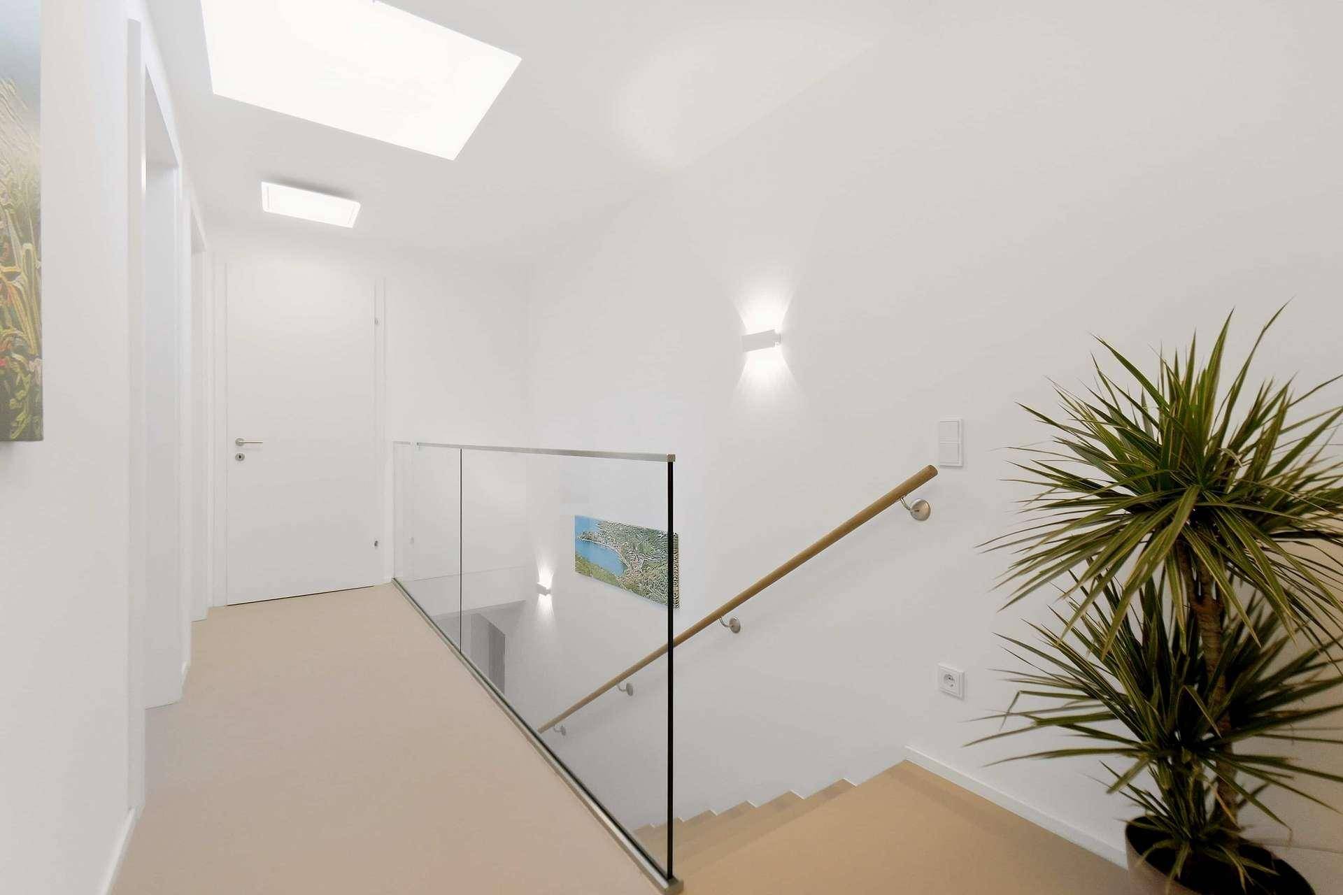 Heller Treppenaufgang mit Glasgeländer und modernem Handlauf, der in die obere Etage führt.