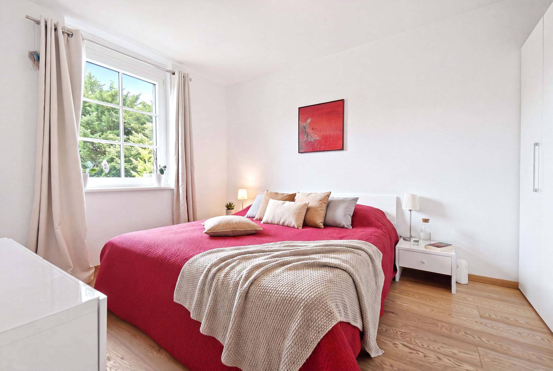 Gemütliches Schlafzimmer mit roter Bettdecke, weißem Kleiderschrank und Holzboden, hell und freundlich.