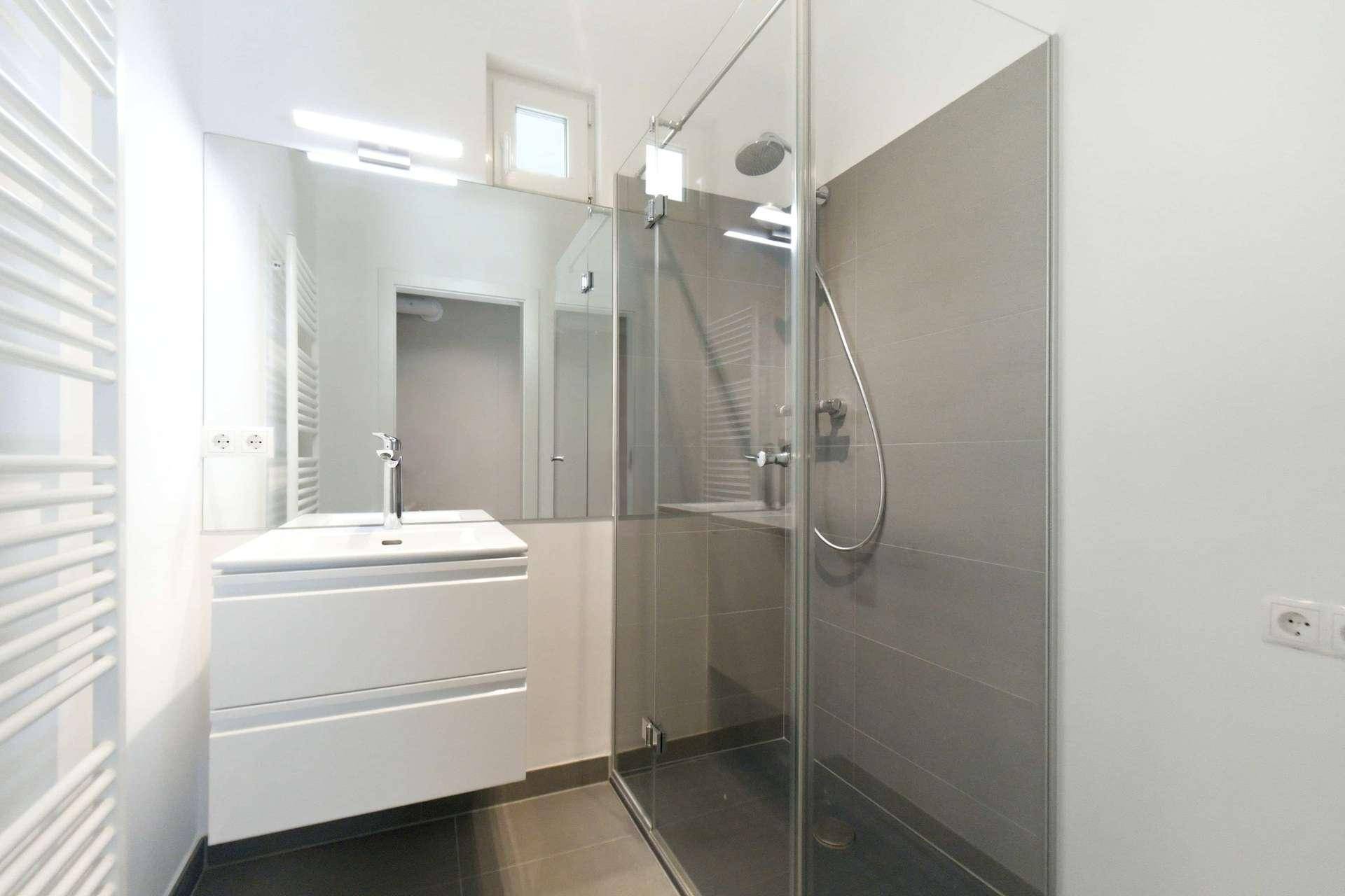 Modernes Badezimmer mit begehbarer Dusche, großem Spiegel und beheiztem Handtuchhalter.