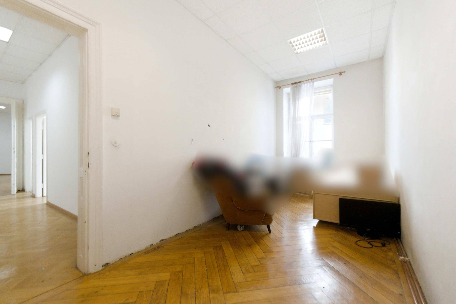 Kleiner Raum mit Fischgrätparkett und einem Fenster, teilweise möbliert mit Sessel und Schreibtisch.