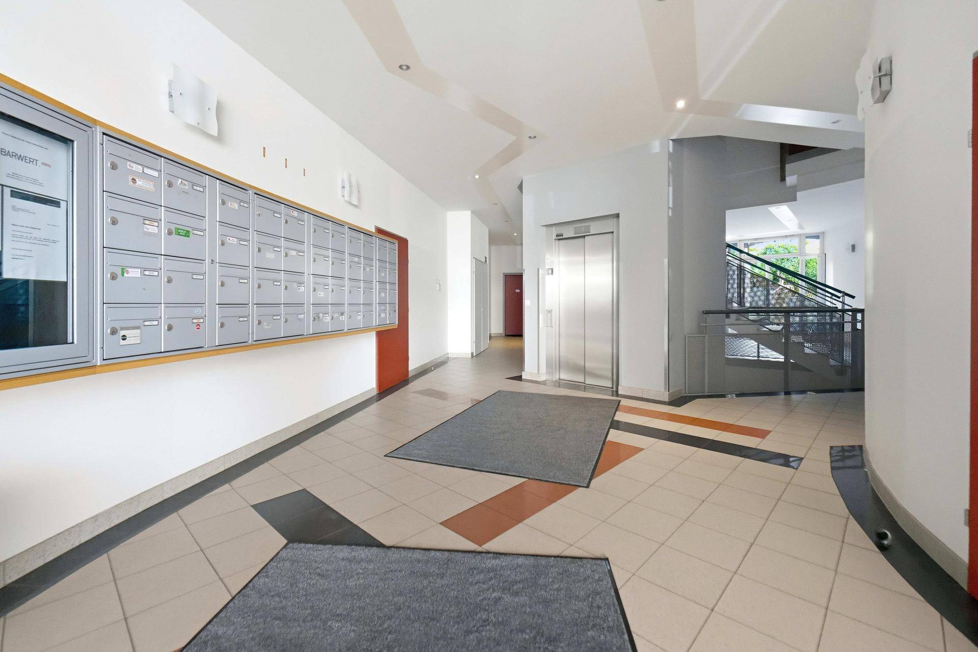 Heller Eingangsbereich mit Fliesenboden, Briefkästen und Zugang zum Aufzug und Treppenhaus.