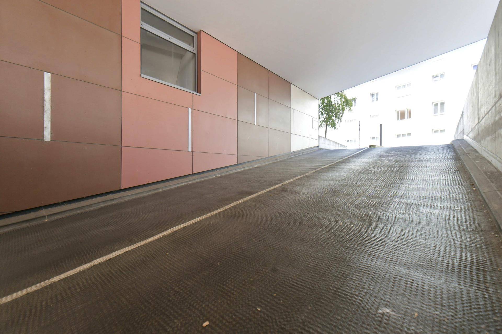 Einfahrtsrampe zu einer Tiefgarage mit geriffelter Oberfläche und moderner Wandverkleidung.