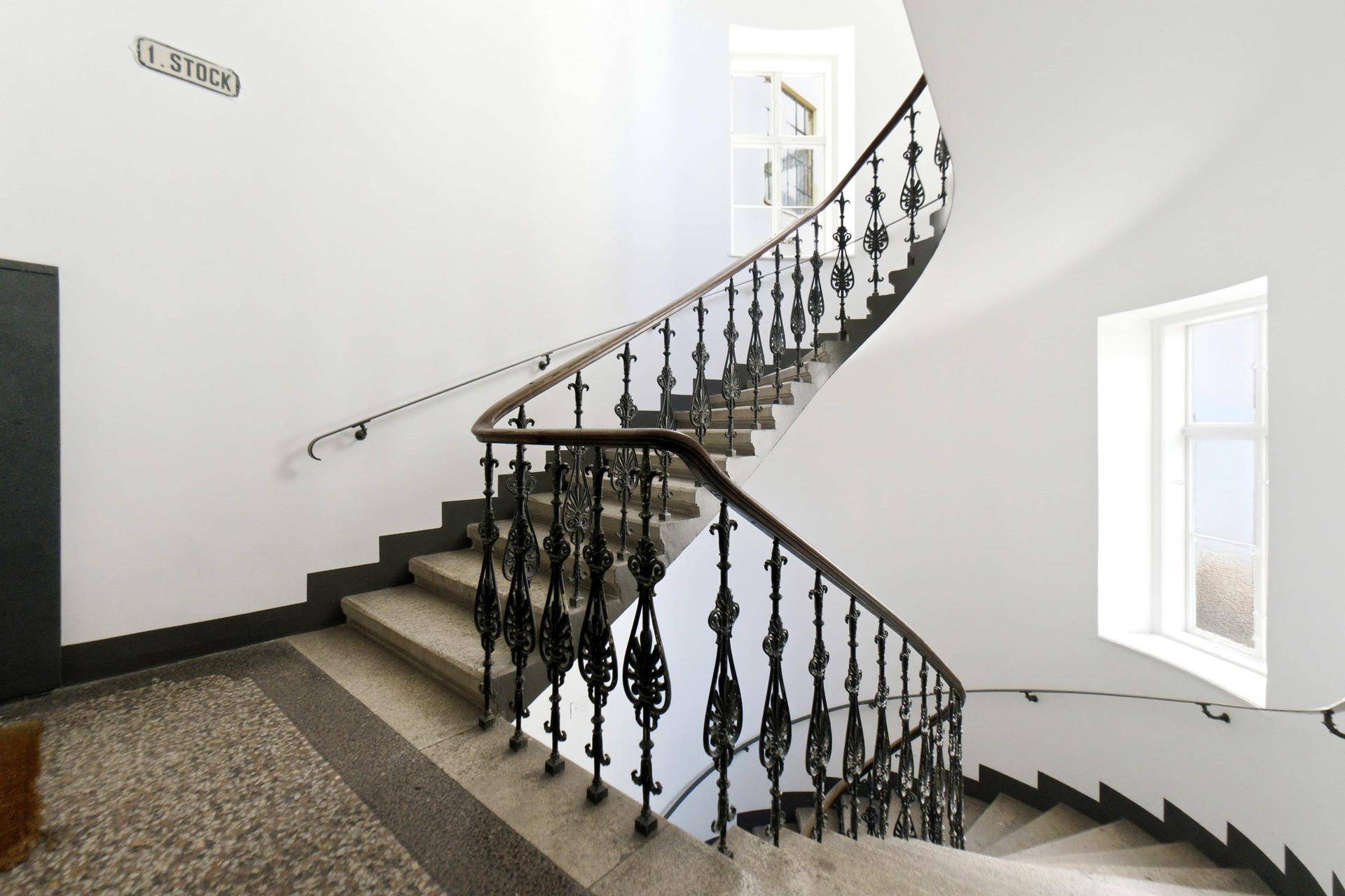 Elegantes Treppenhaus in einem Altbau mit geschwungenem Geländer und Tageslicht.
