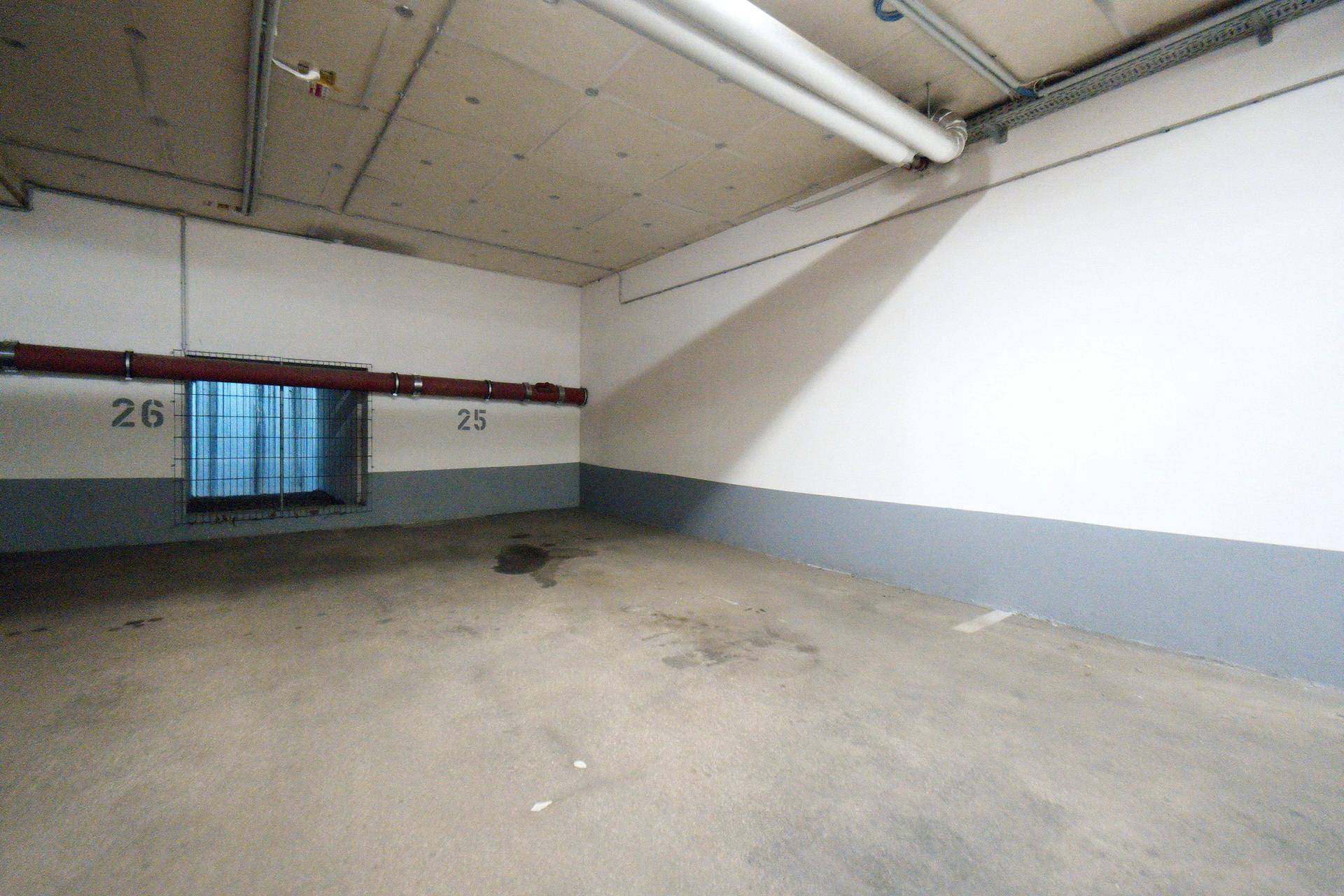 Leerer Stellplatz in der Tiefgarage mit Betonboden und Gitterfenster zur Belüftung.