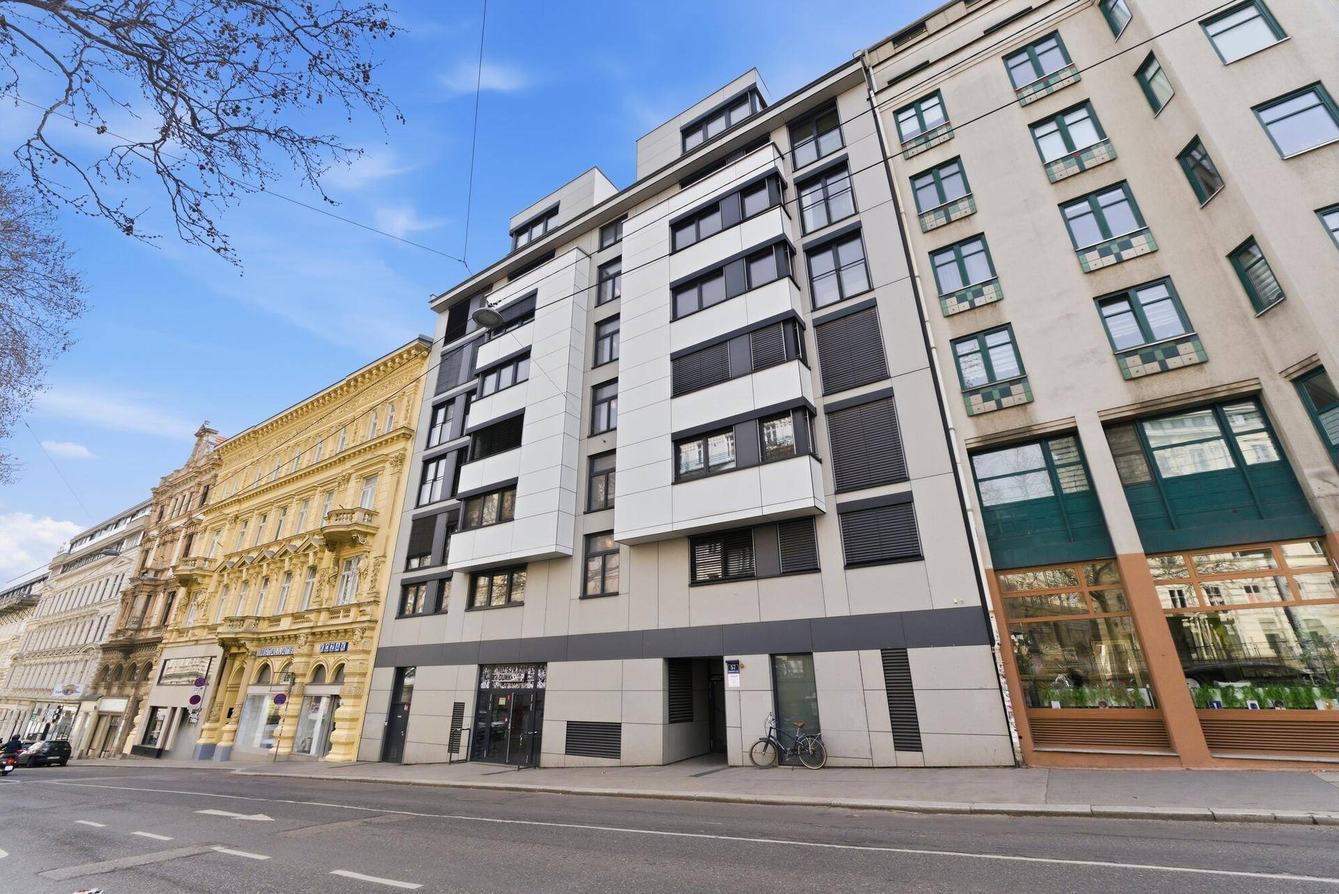 Moderne Wohnhausfassade an einer Stadtstraße, umgeben von traditioneller Architektur.