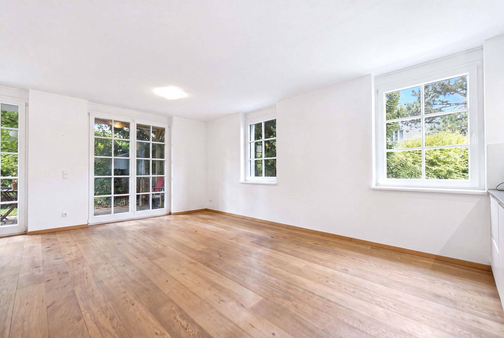 Geräumiger, leerer Wohn-Essbereich mit Holzboden und großen Fenstern zum Außenbereich.