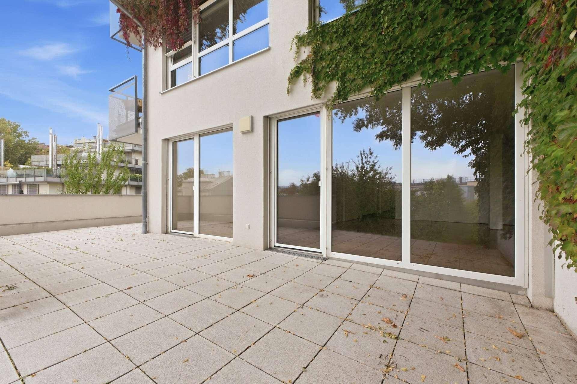 Geräumige Außenterrasse mit Fliesenboden und großen Glasfronten zum Wohnbereich.
