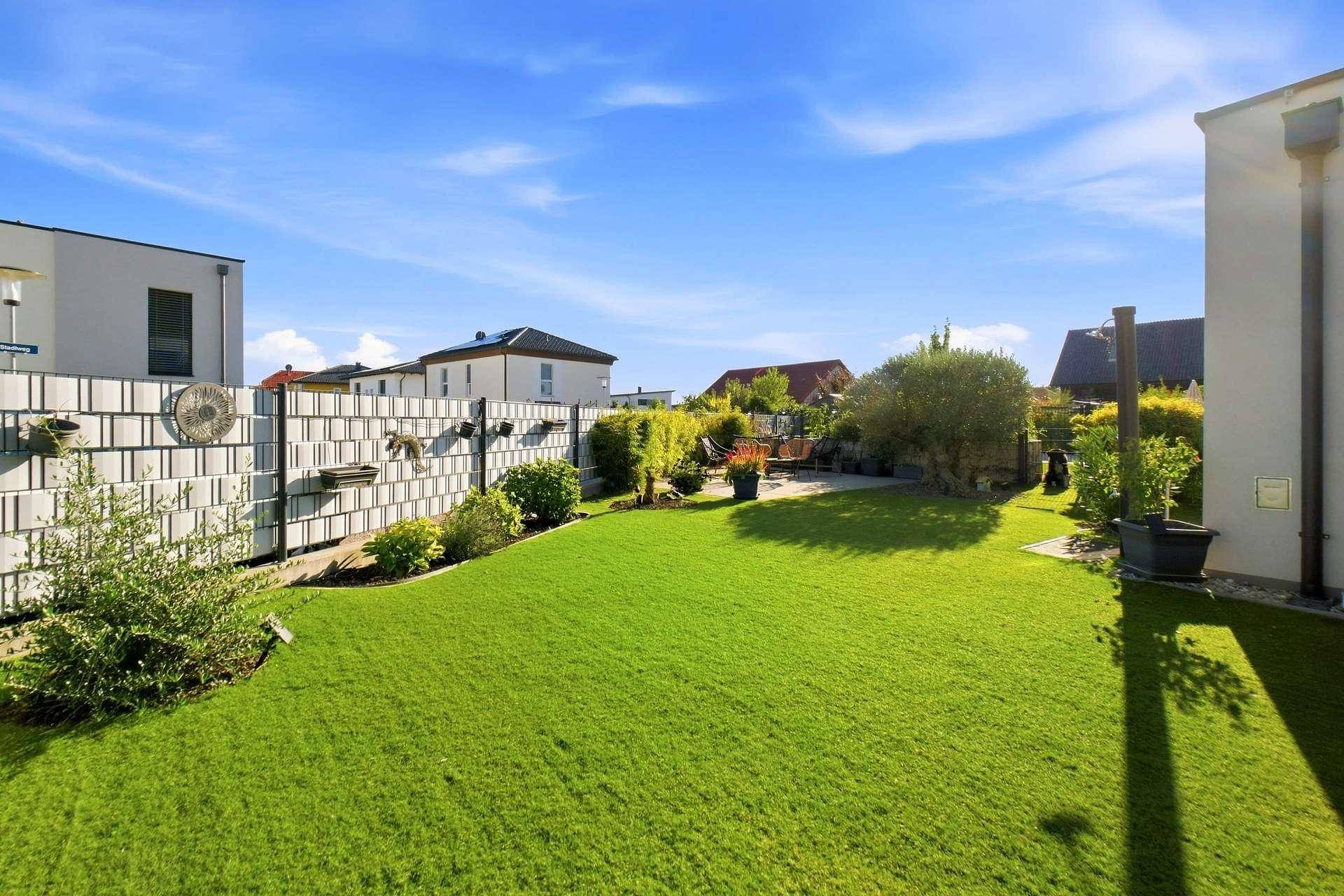 Großer, sonniger Garten mit weitläufiger Rasenfläche und grüner Hecke.