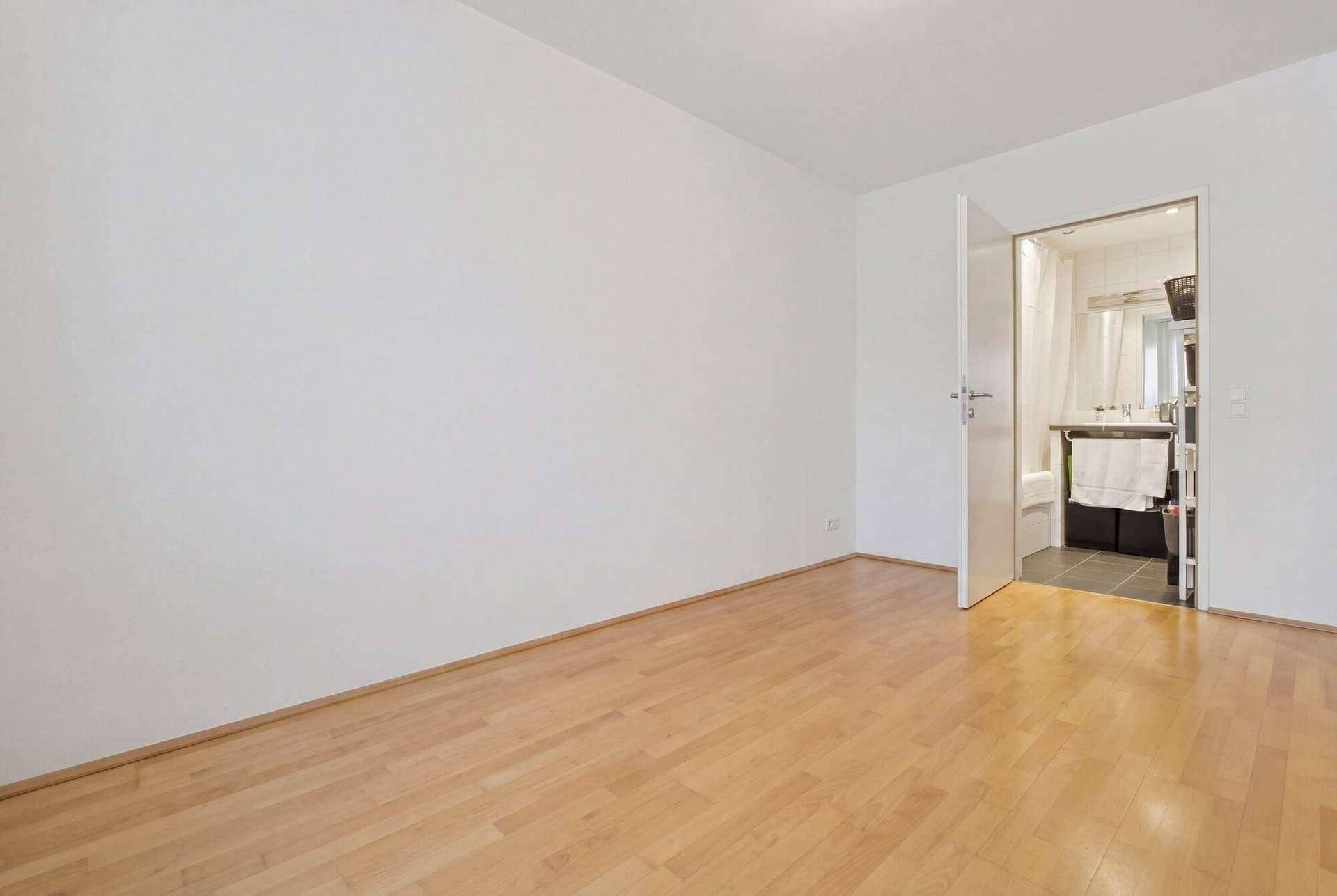 Leeres Schlafzimmer mit Parkettboden und Zugang zu einem angrenzenden Badezimmer.