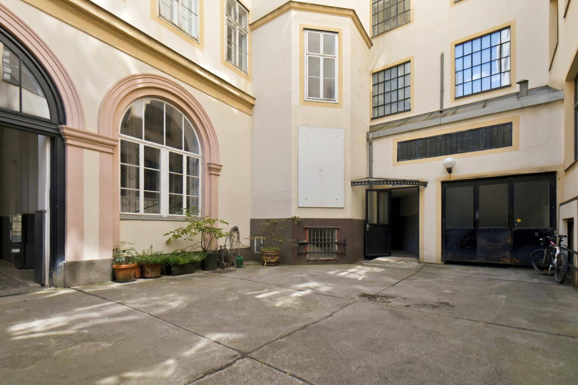 Heller Innenhof mit gepflastertem Boden und großen Fenstern, umgeben von Gebäudefassaden.